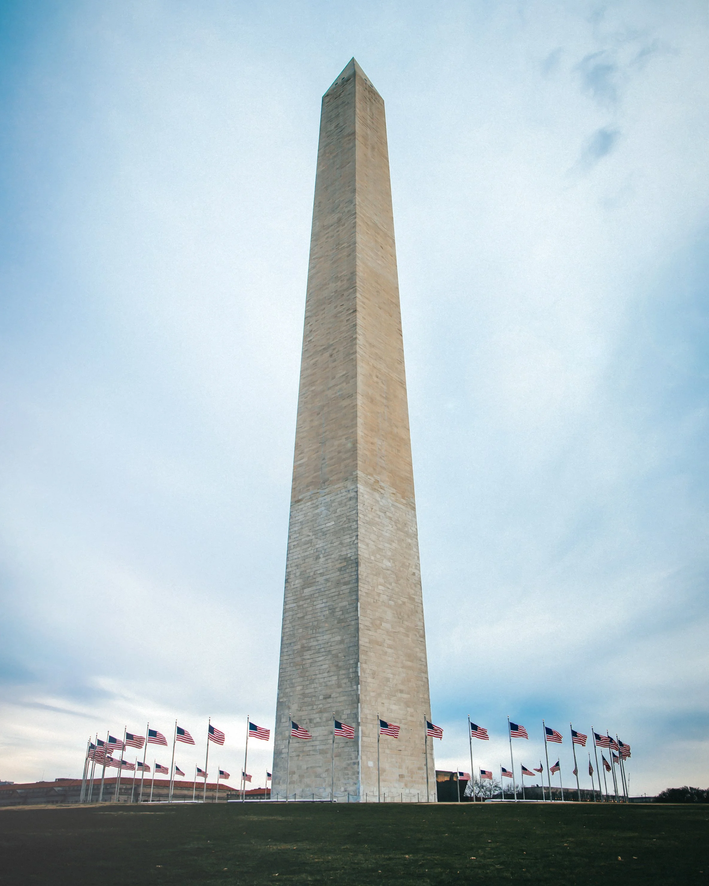 Washington Monument in Washington, D.C., with American flags surrounding its base and a cloudy sky