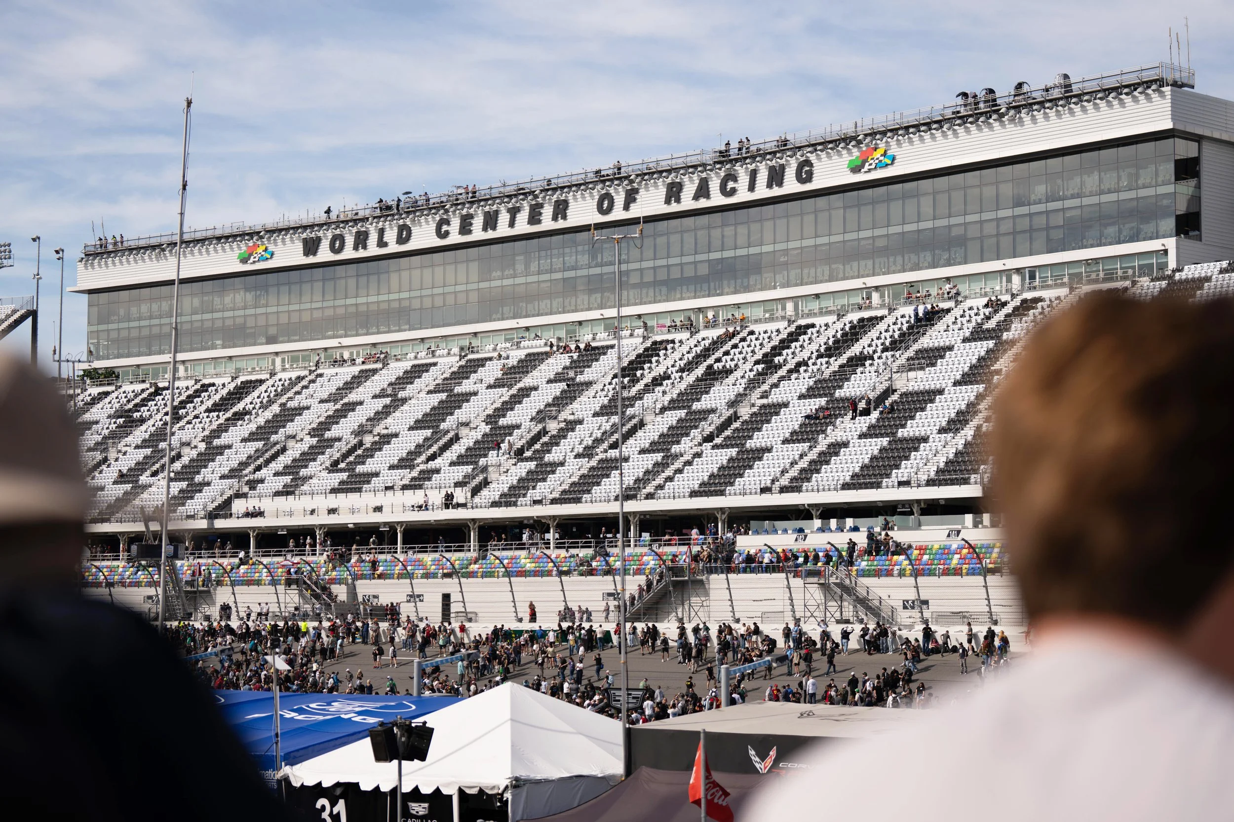 Exterior view of the World Center of Racing at a racetrack with a large crowd and seating in the foreground.