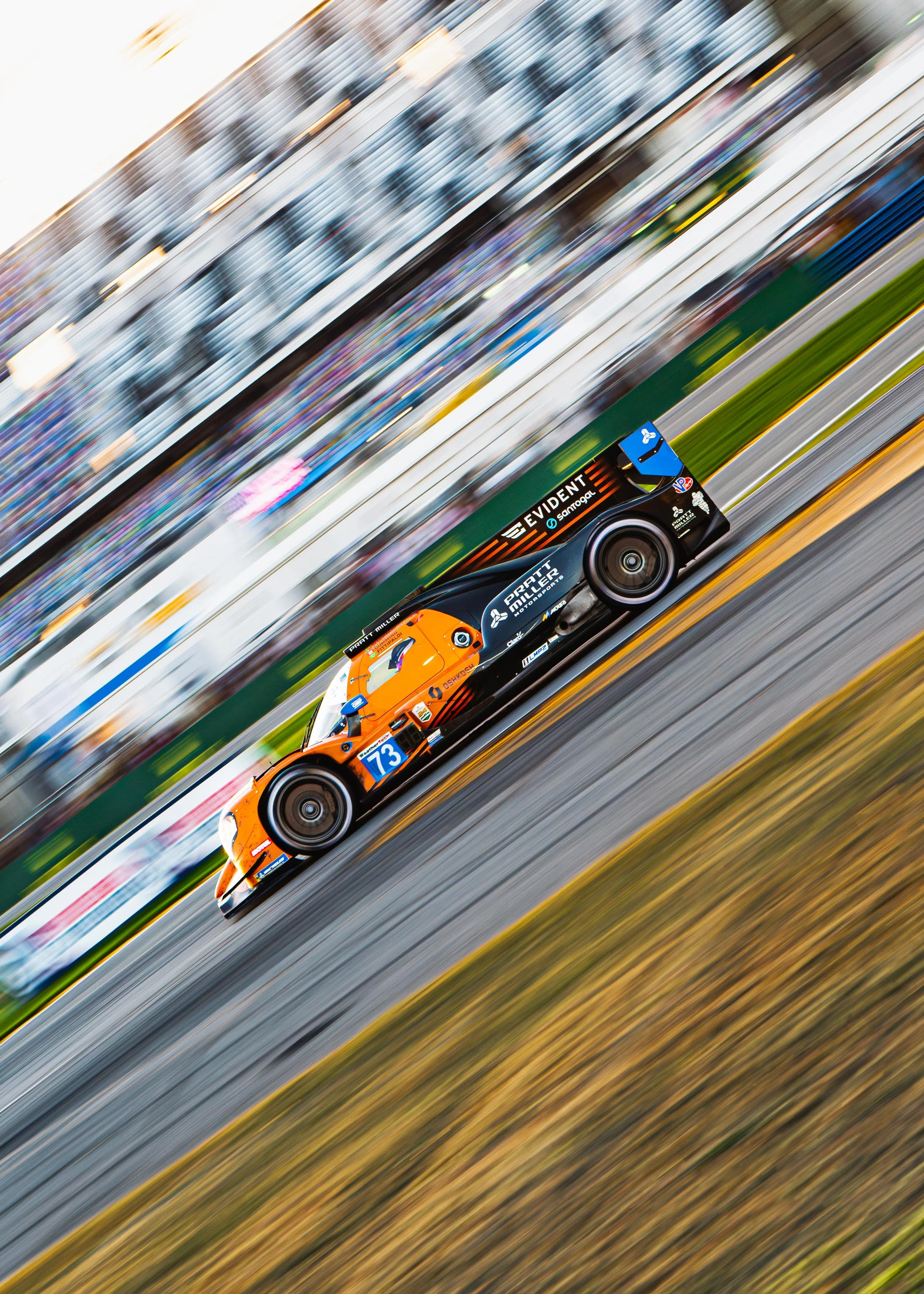 A race car on a track in motion, with blurred background and streaks of color, number 73, orange and black livery.