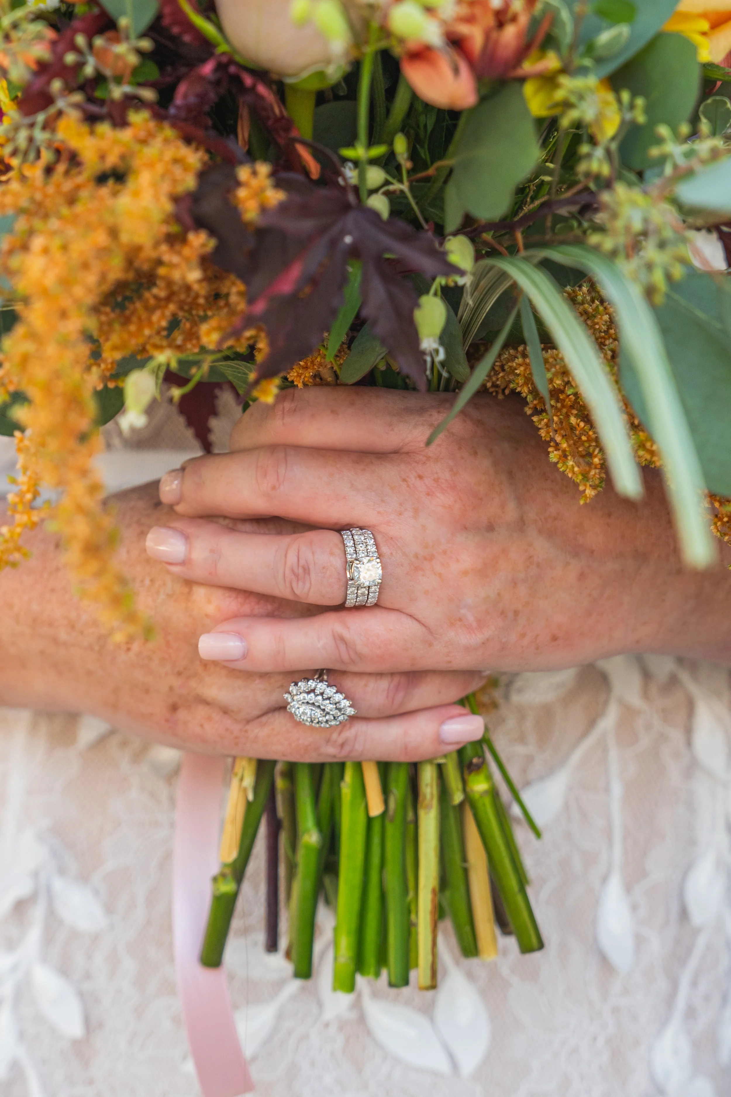 Bride holding a colorful bouquet of flowers, wearing multiple diamond rings on their fingers.