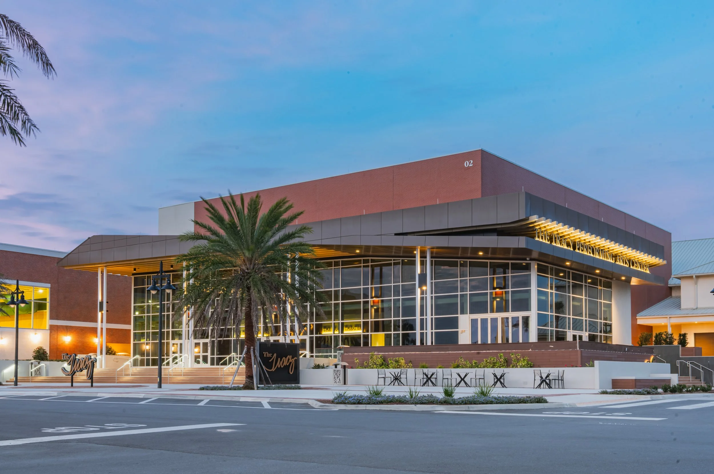Exterior of the Performing Arts Center with large glass windows, a palm tree in the front, and a modern architectural design, taken at dusk.
