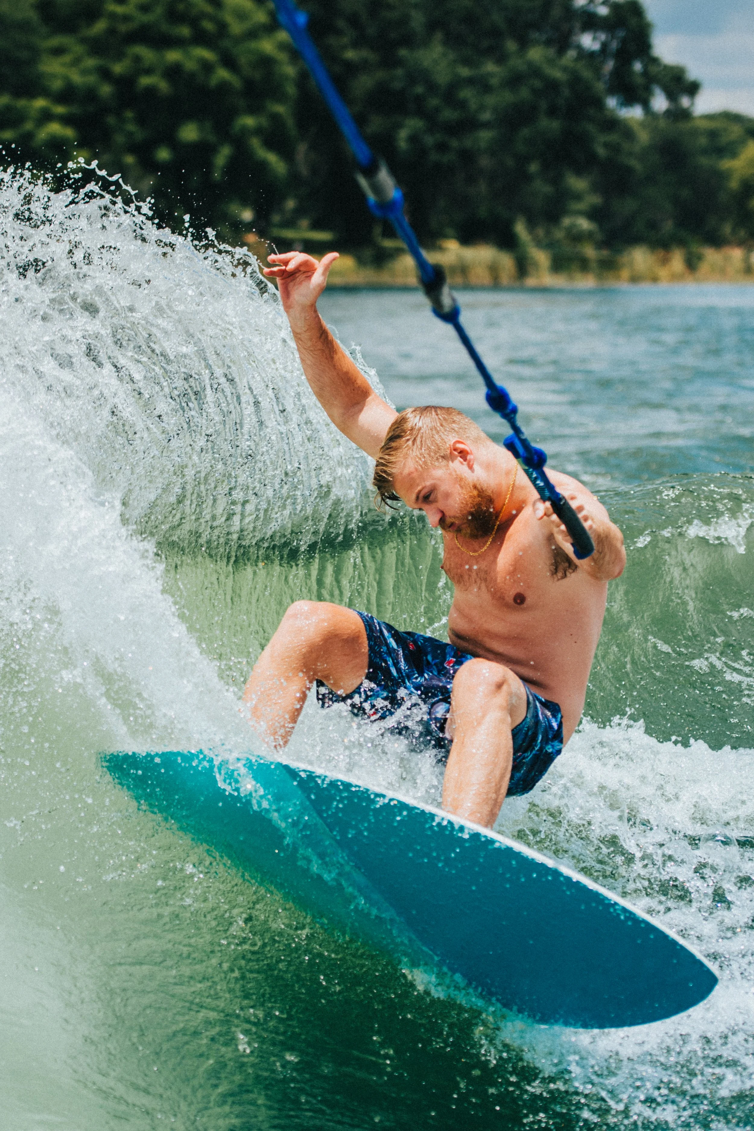 A man surfing on a wave in a body of water, with a shoreline and trees in the background.