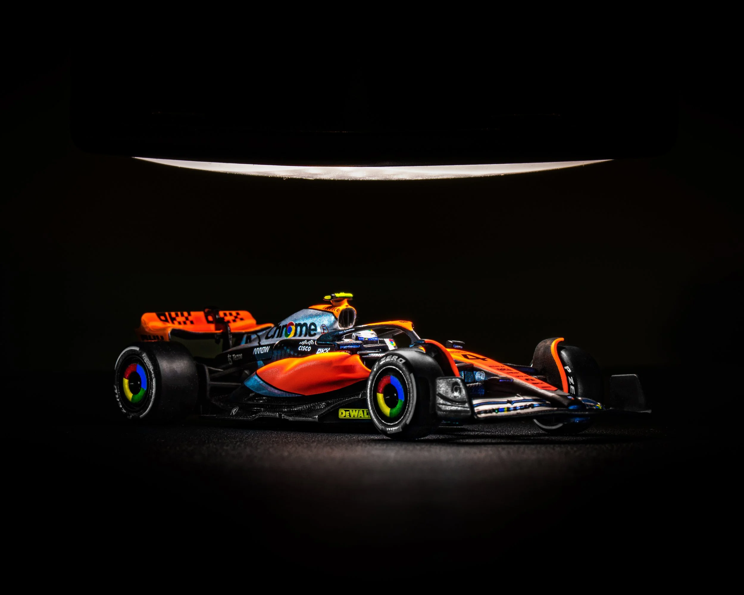 A high-performance McLaren Formula 1 racing car with orange, black, and blue colors, featuring sponsor logos including Google, under a bright light in darkness. Lando Norris racecar. 