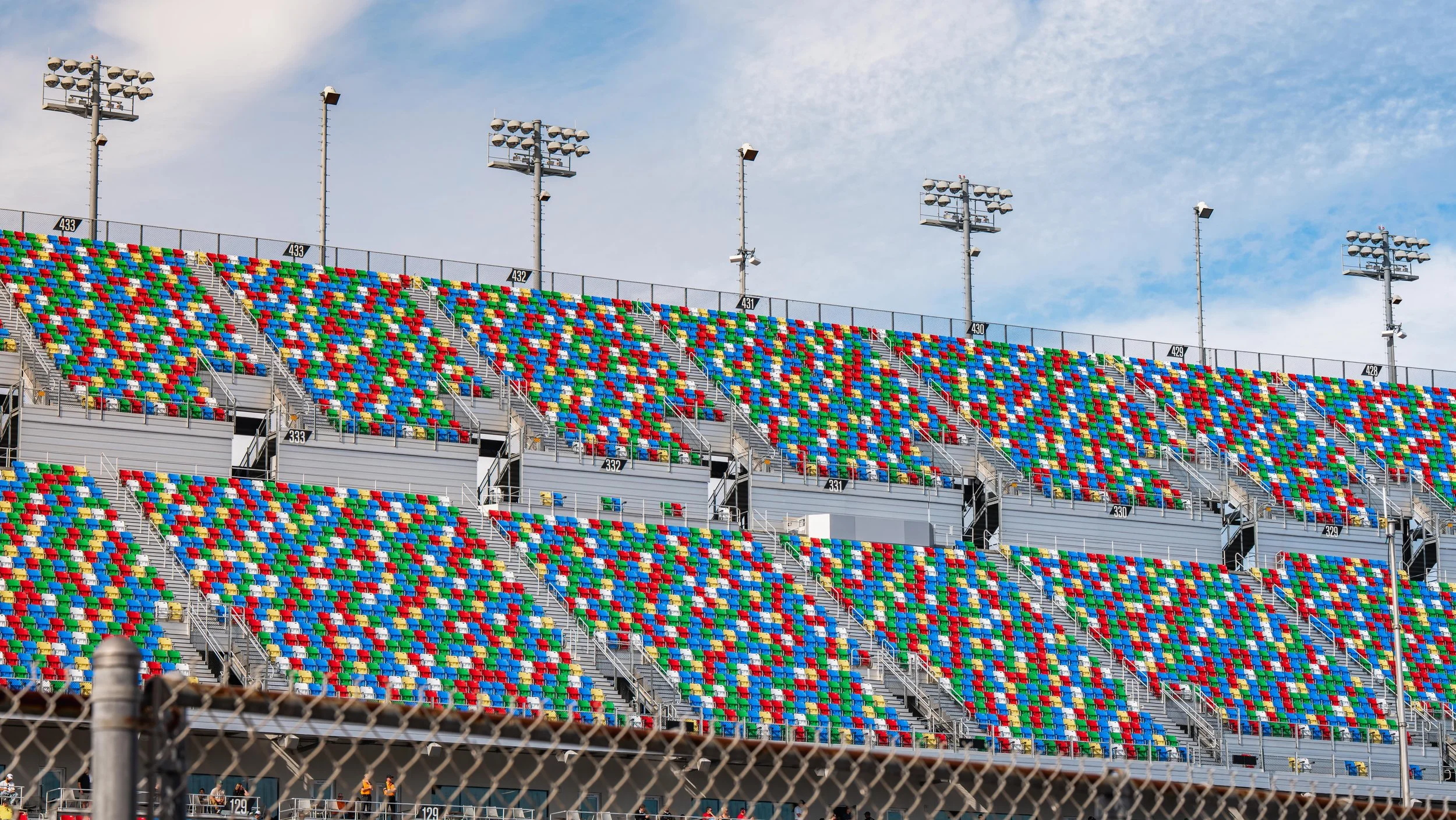 Empty race track stands with colorful seats in red, blue, green, and yellow, under a partly cloudy sky.