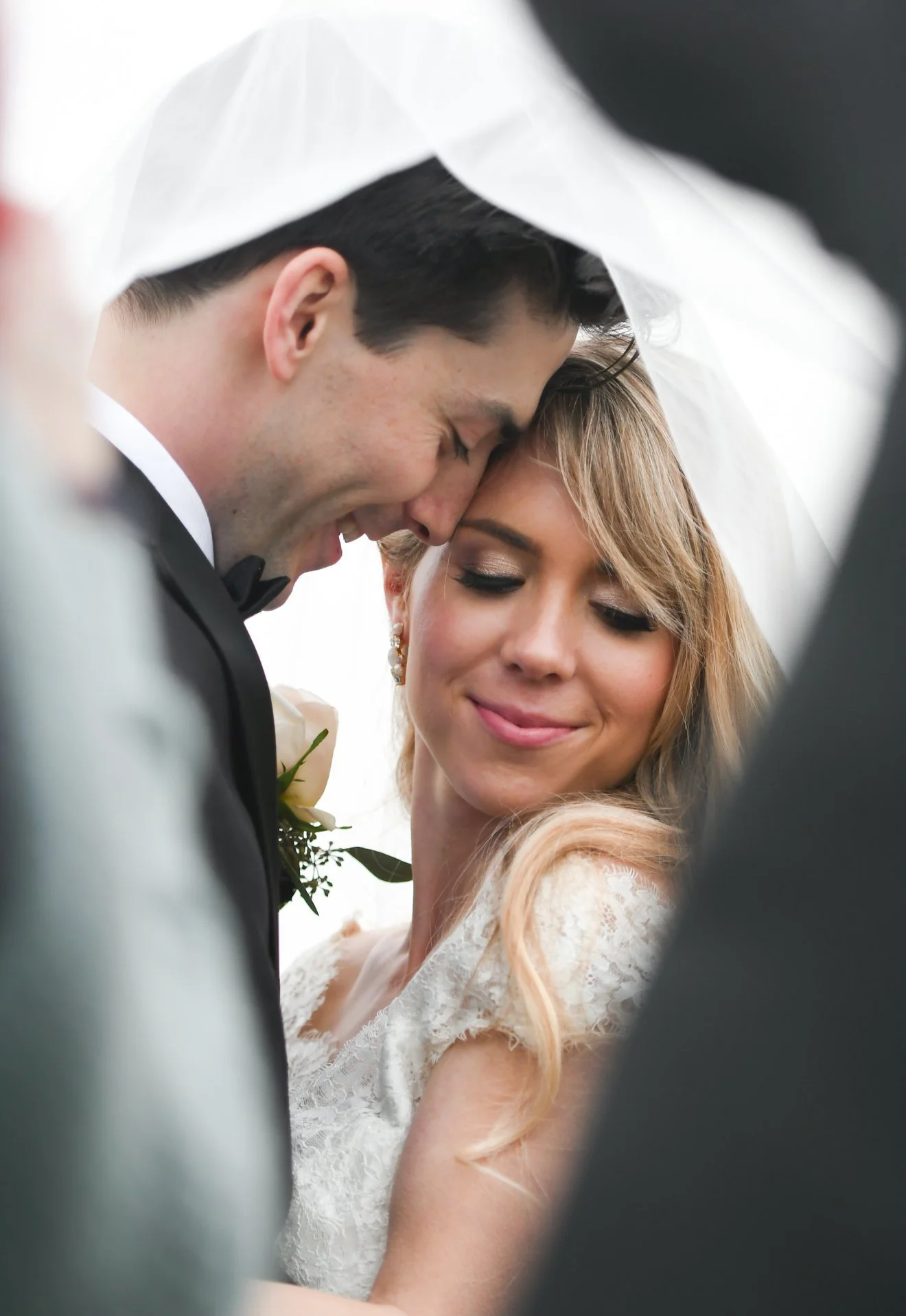 Close-up of a newlywed couple smiling with foreheads touching under a white veil.
