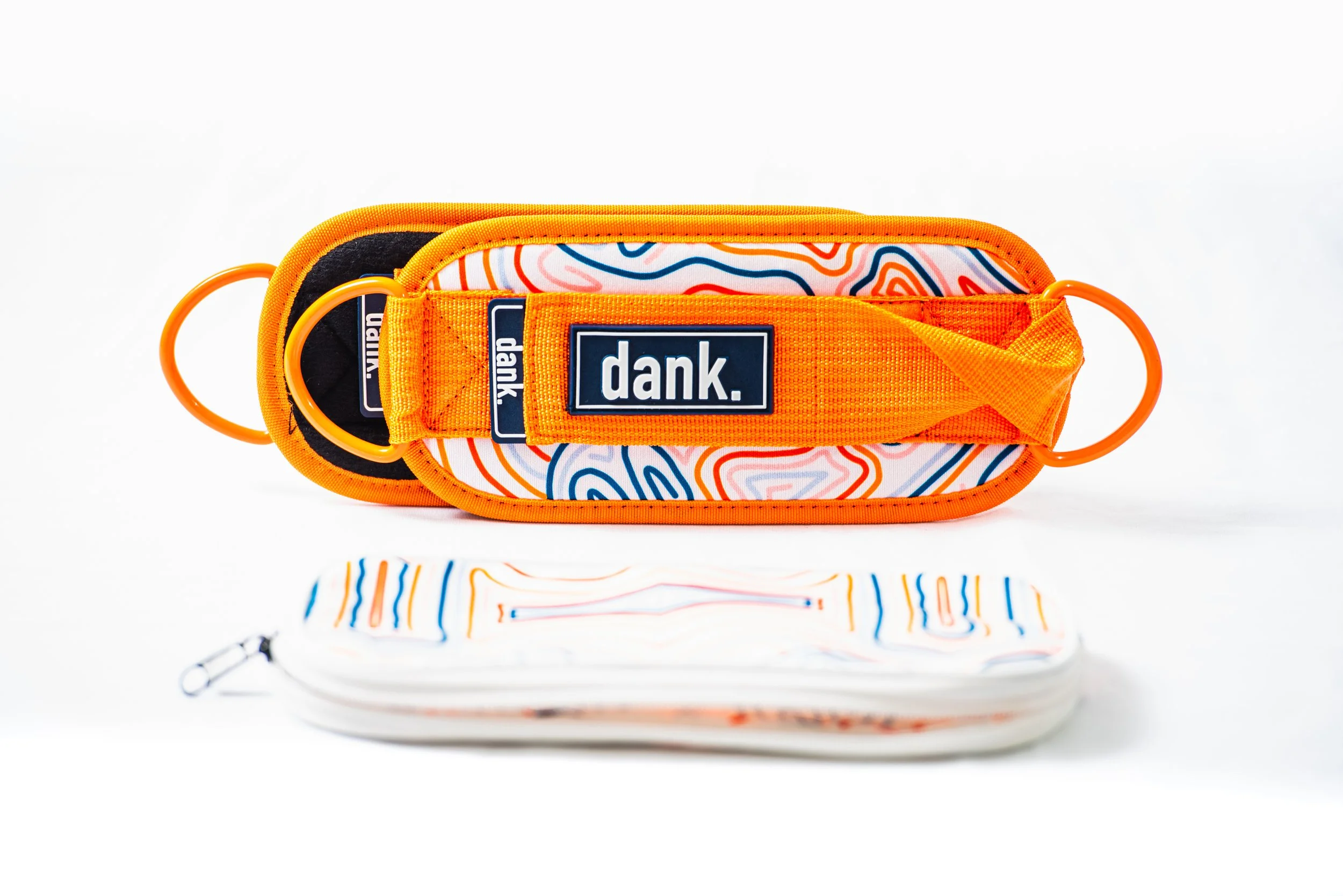 DANK Athletics. Colorful waist bag with orange accents, a thick orange strap with a 'dank.' logo, and a patterned interior, placed on a white background alongside a matching patterned mask.