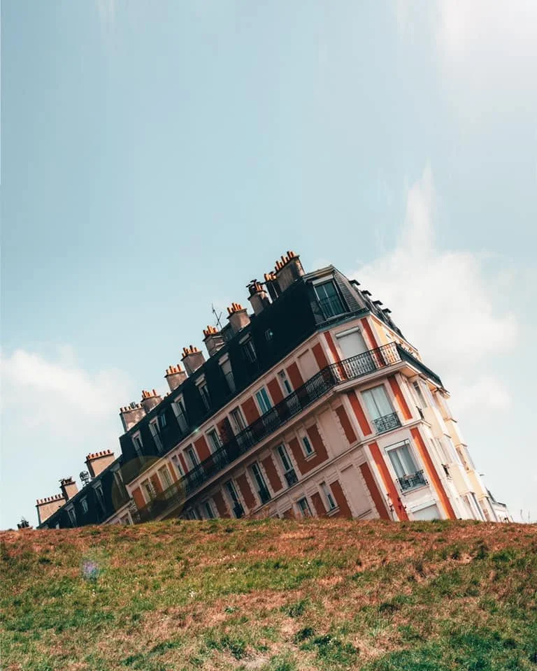 A tilted multi-story residential building on a grassy hill with a partly cloudy sky in the background. Montemarte, Paris ,France.