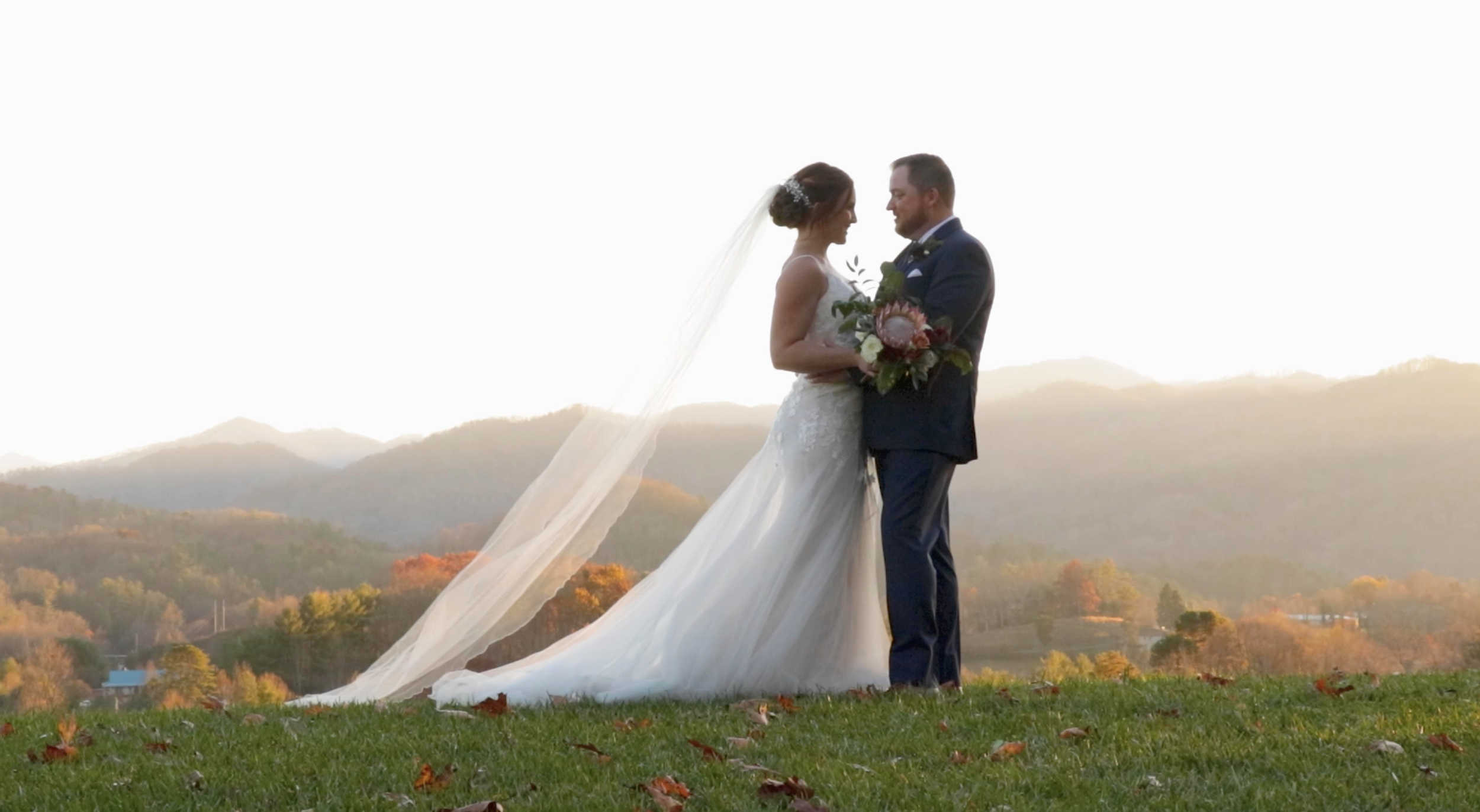 A bride and groom standing close together on a grassy hill with mountains in the background during sunset in Asheville, North Carolina.