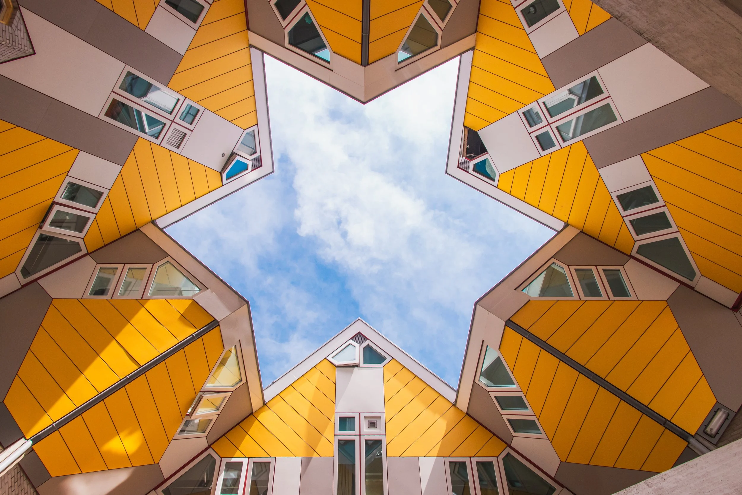 View of a colorful modern apartment building from the ground looking up, with a star-shaped opening in the center revealing the sky. Cube houses Rotterdam, Netherlands. 