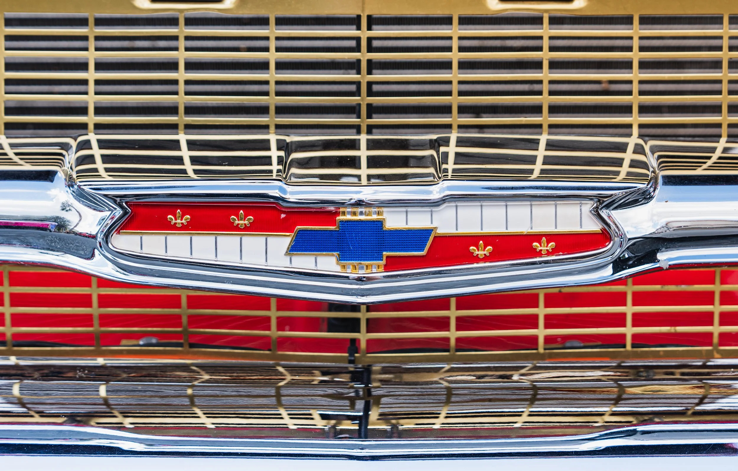 Front of vintage Chevrolet car with chrome grille, Chevrolet emblem, and decorative fleurs-de-lis on a red background.