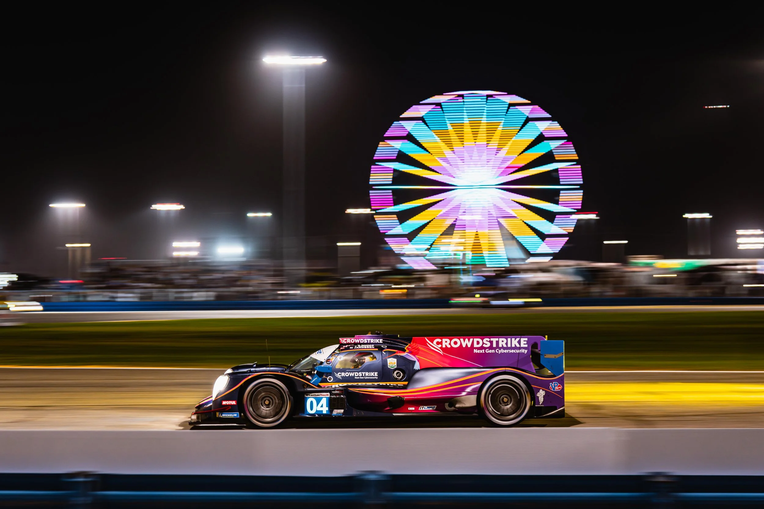 Race car on track at night with illuminated Ferris wheel in the background.