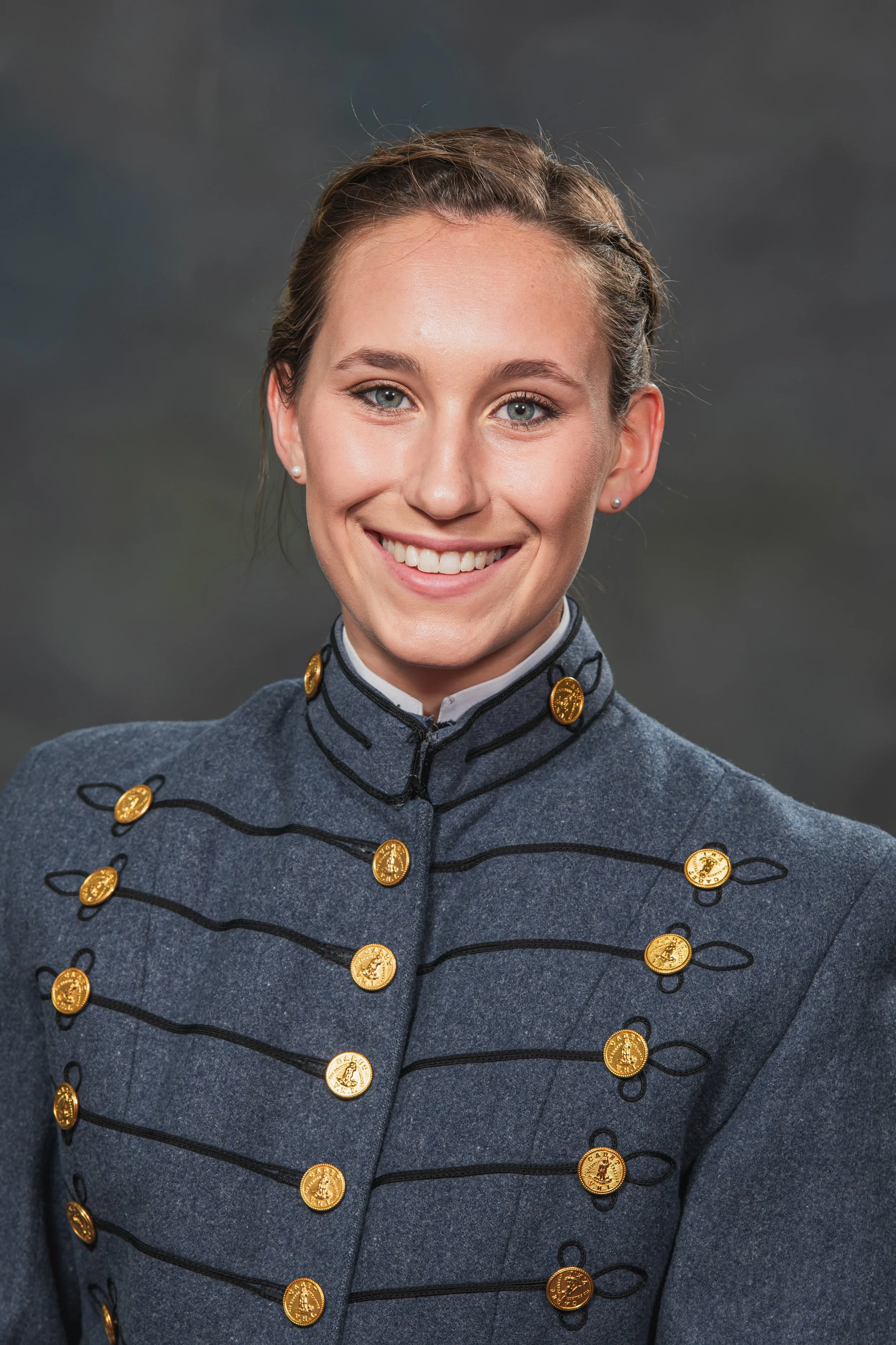 A woman in a gray military-style uniform with gold buttons smiling at the camera.