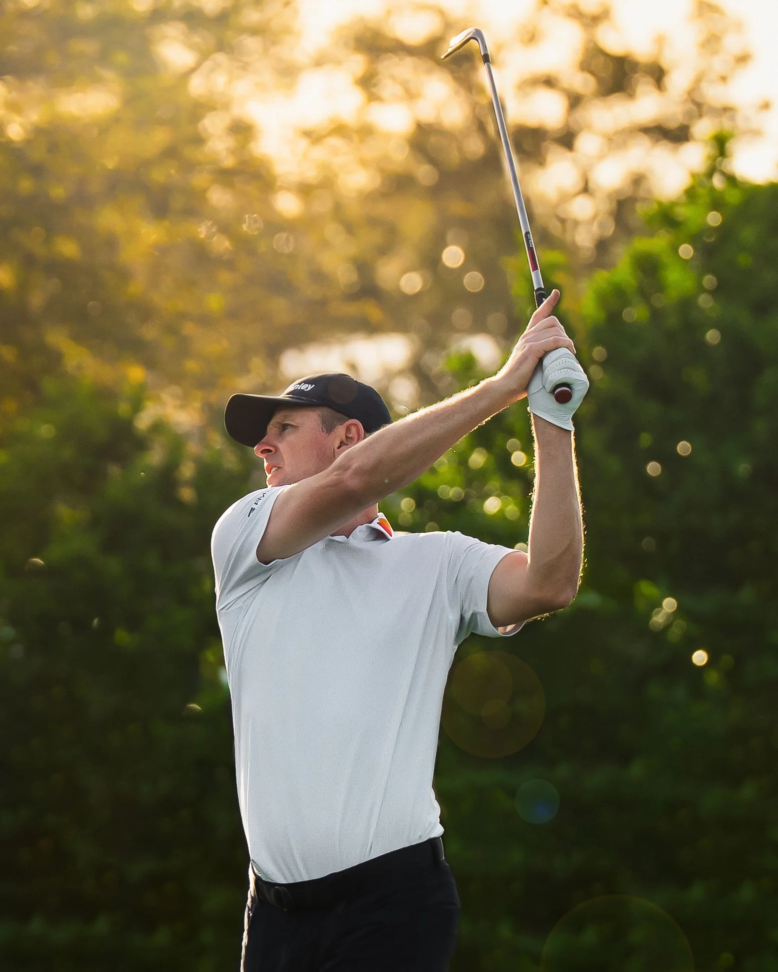 Justin Rose golfer swinging a golf club on a golf course, with trees and sunlight in the background.