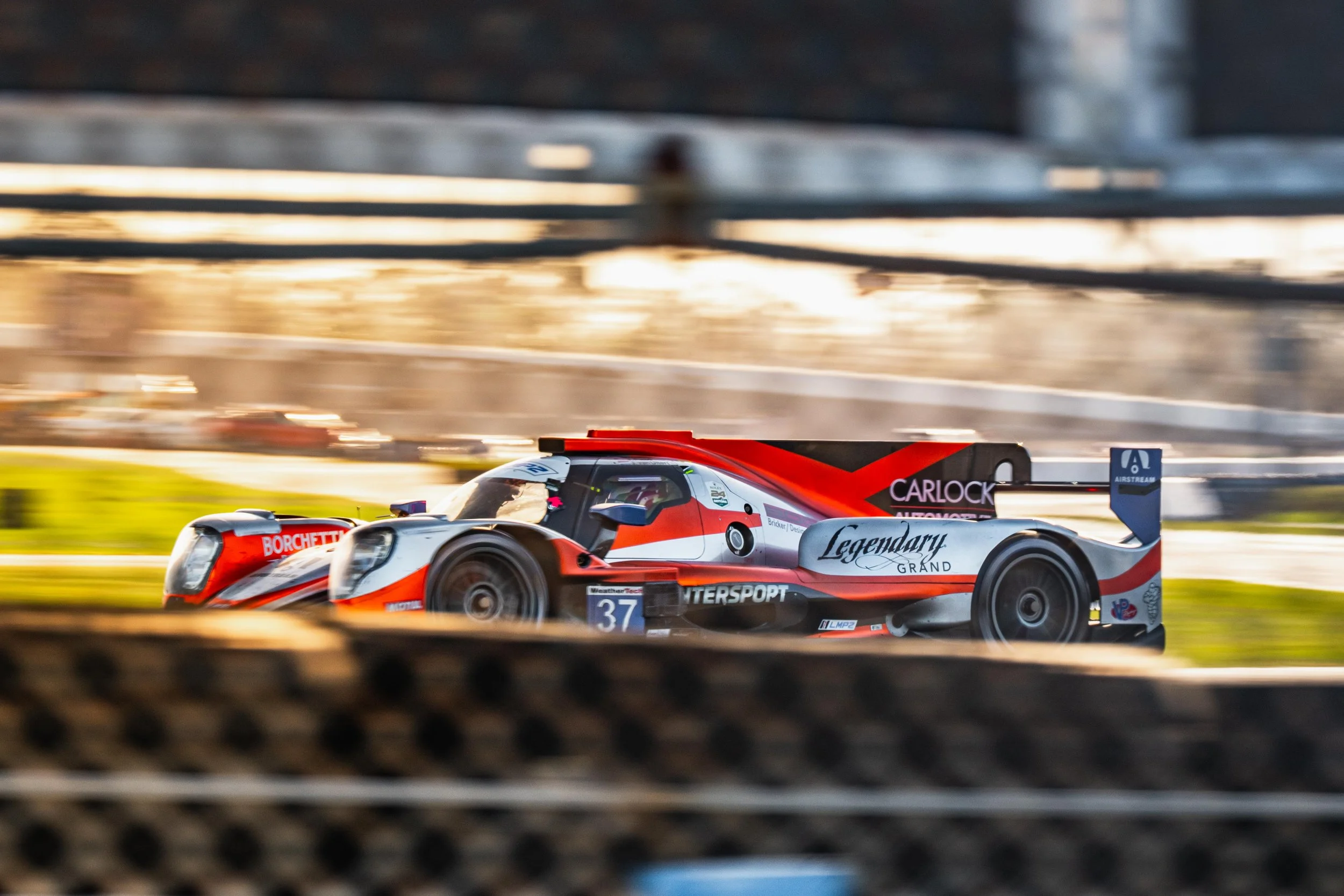 Race car on track, moving quickly, with blurred foreground and background, red, white, and black with sponsorship logos.