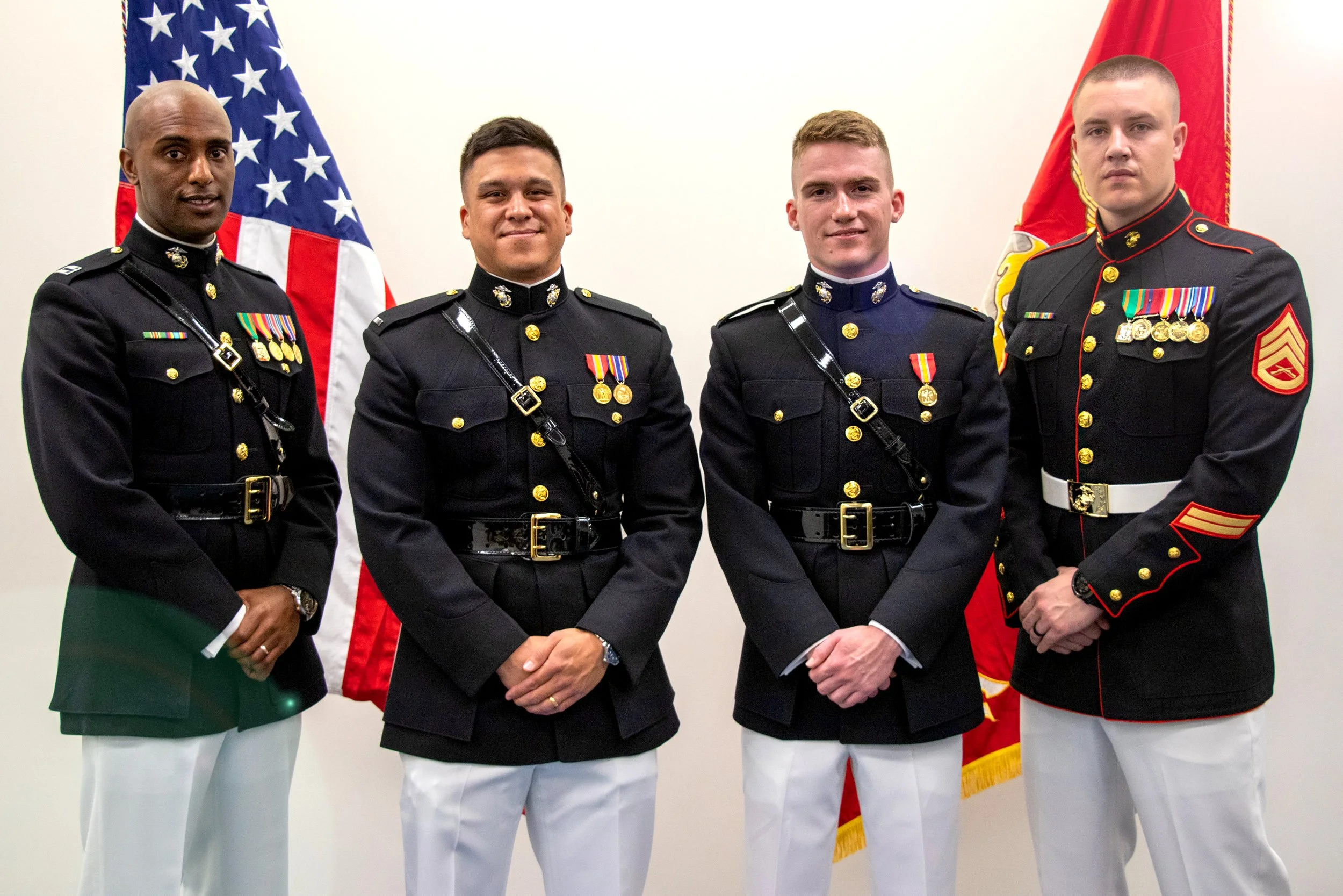 Four military personnel in dress uniforms standing in front of American and Marine flags. Commissioning ceremony. 