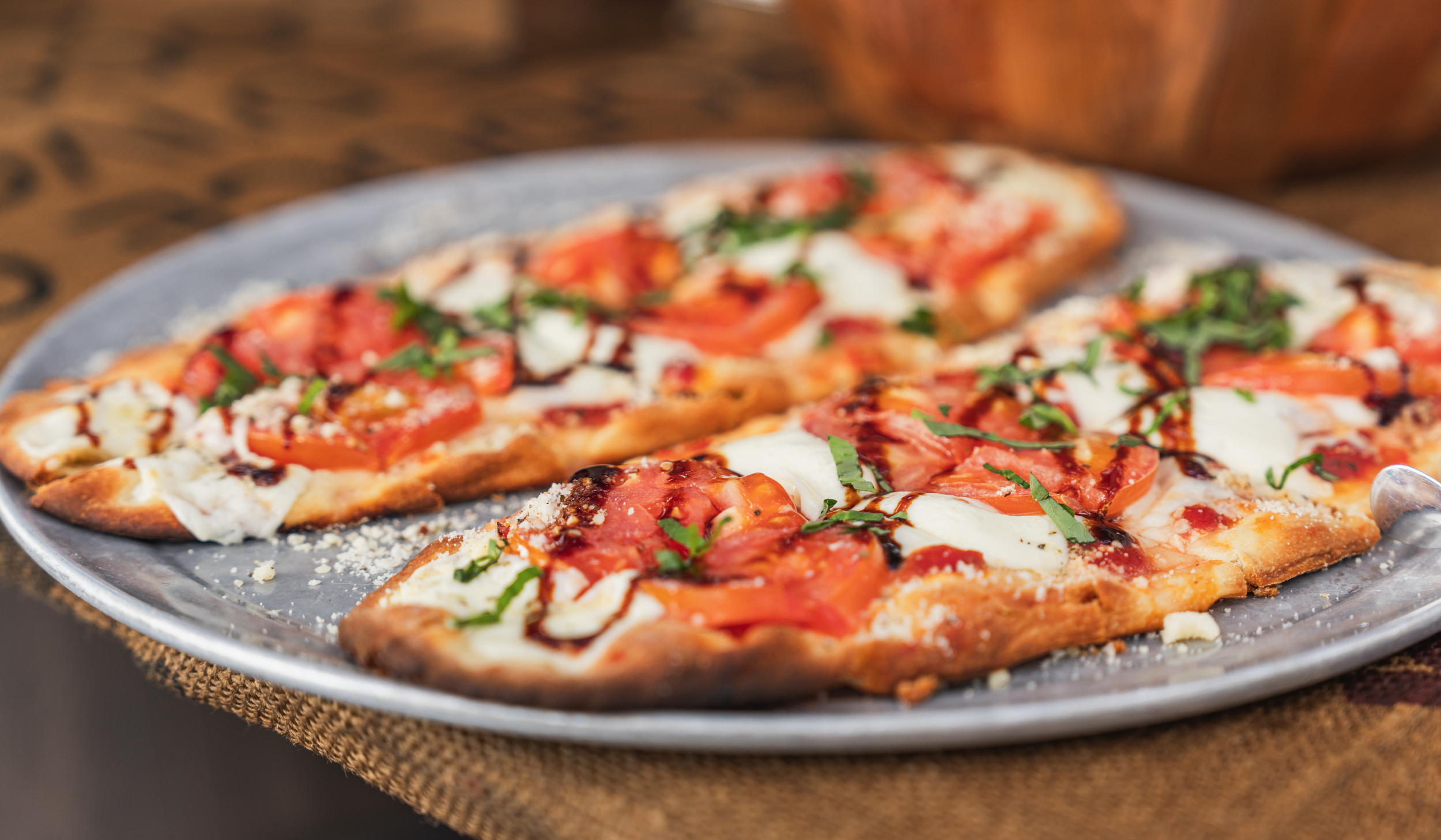 Slices of pizza with tomato, cheese, basil, and balsamic glaze on a gray plate.
