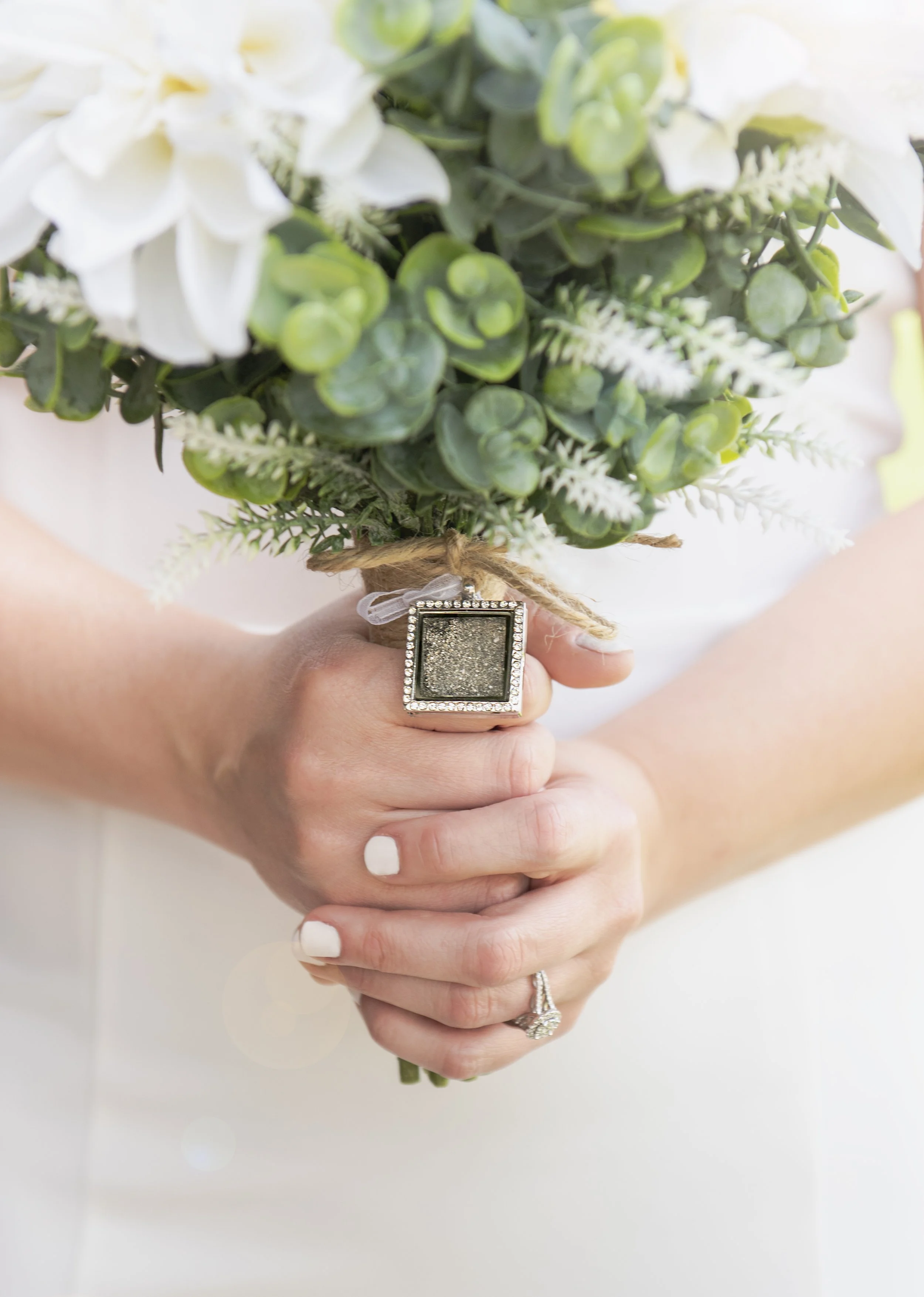 Close-up of a woman's hands holding a bouquet of white flowers and green foliage, with a sparkling ring on her finger and a decorative ring on her other hand.