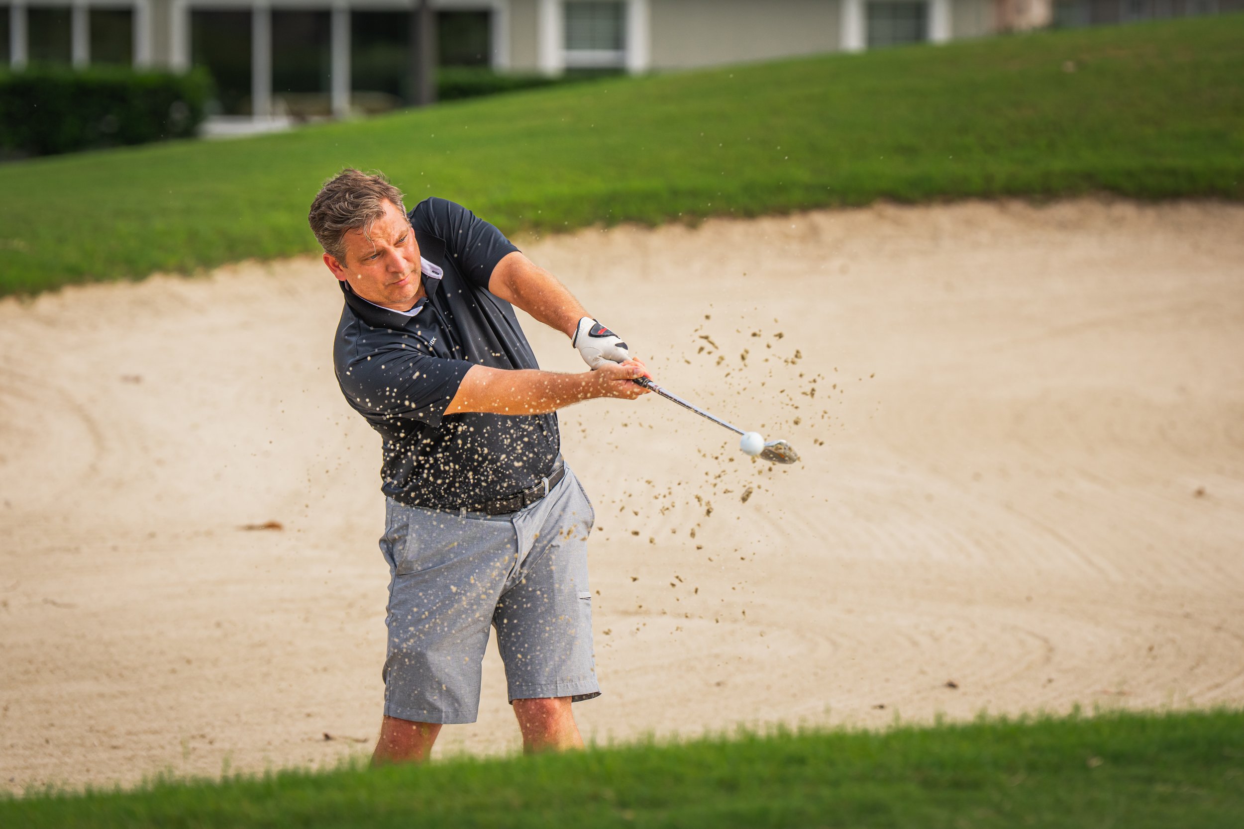 A man playing golf, hitting a golf ball out of a sand bunker on a golf course.