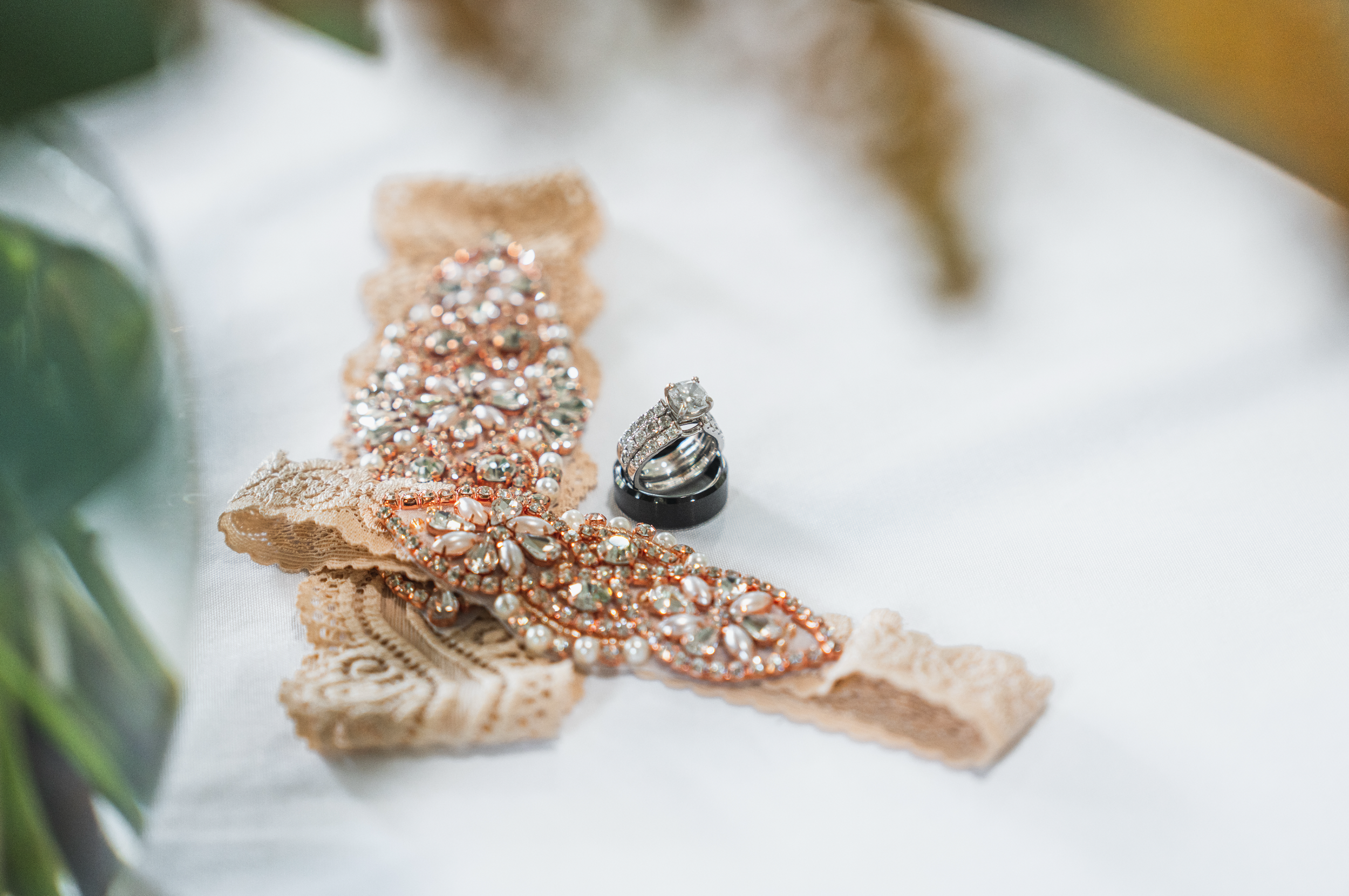 A lace ribbon with an ornate gemstone brooch and a men's wedding ring with diamond accents on white fabric.