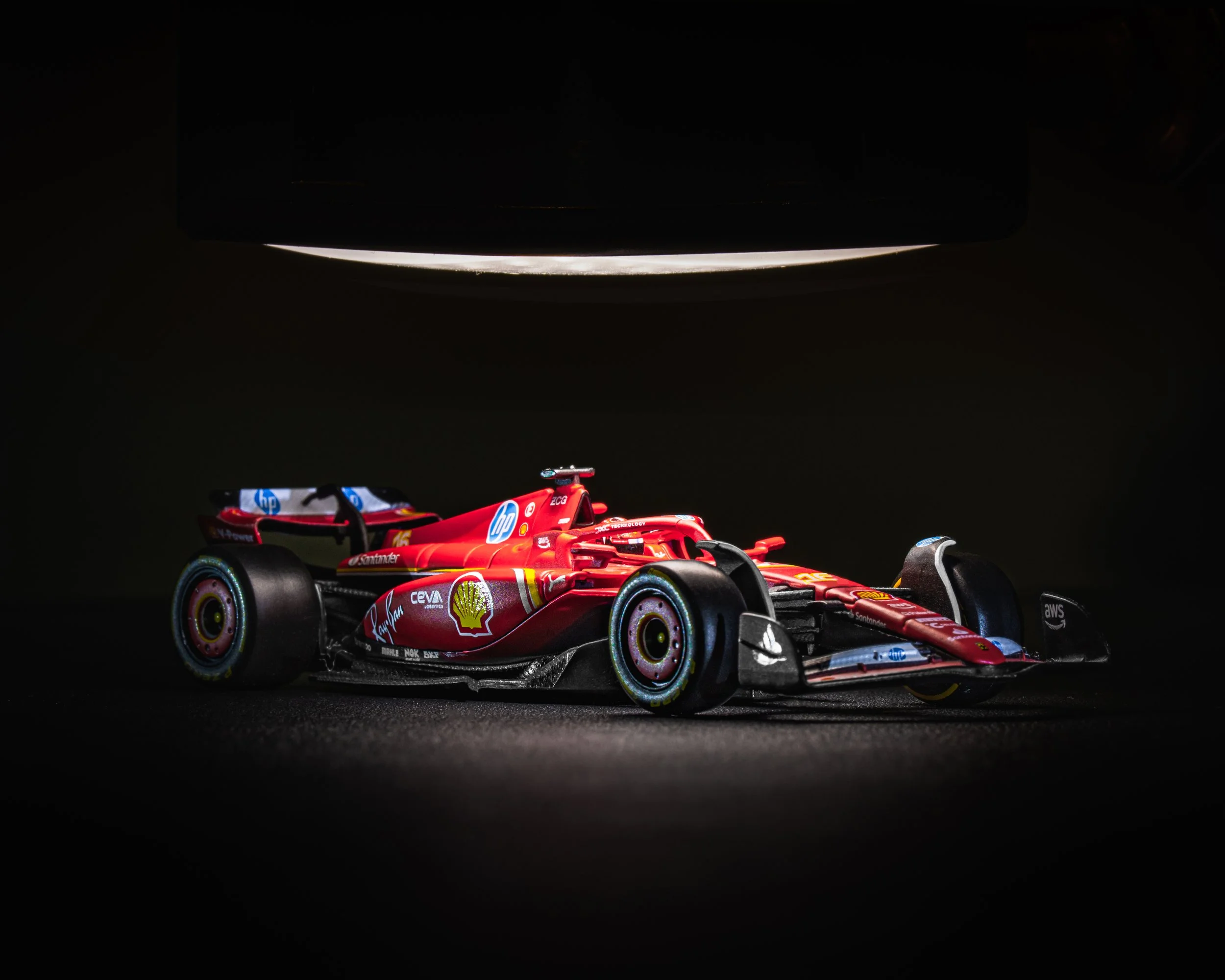 A detailed close-up of a red Formula 1 Ferrari race car with sponsor logos, illuminated under a focused light against a dark background. Charles Leclerc racecar.