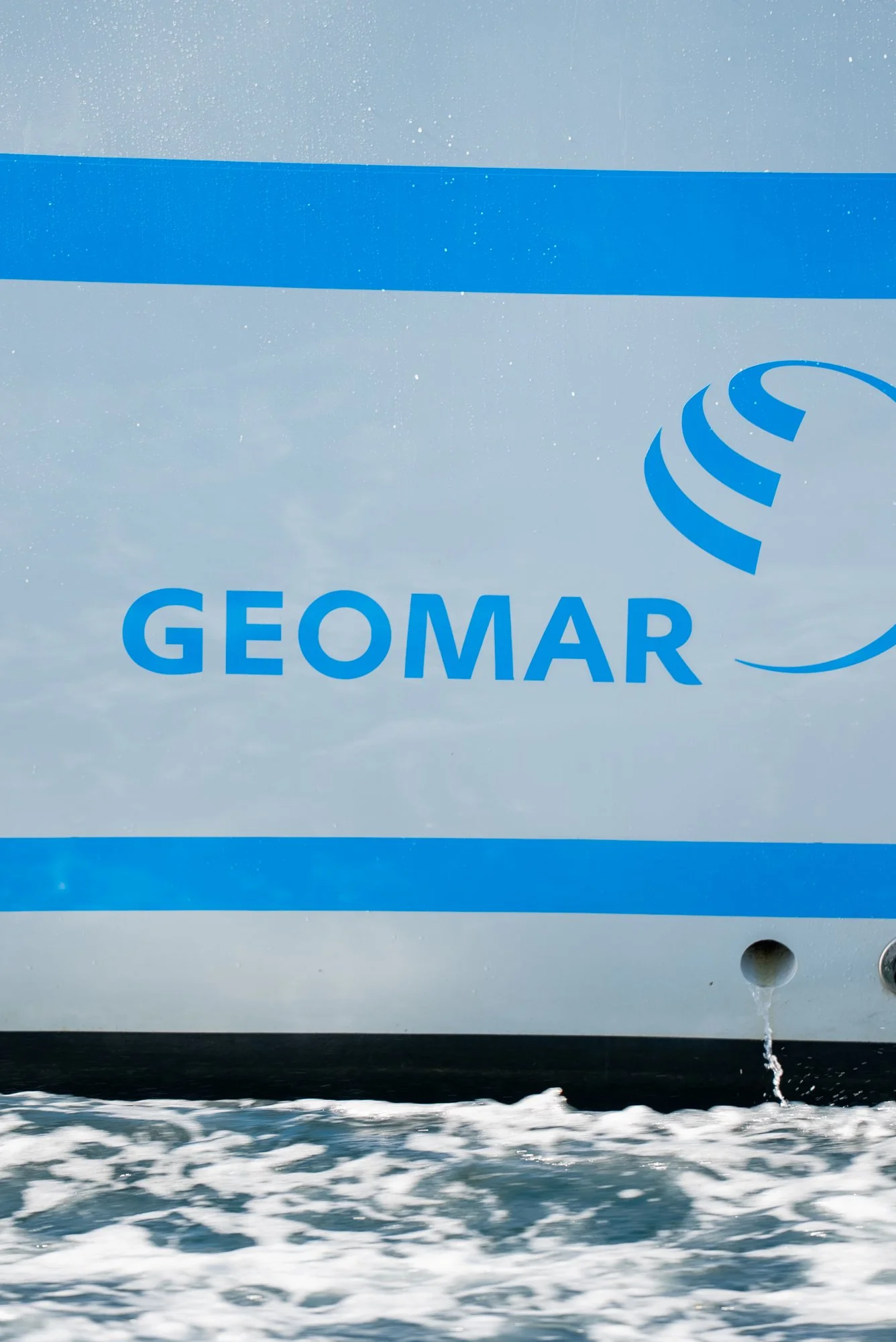 Close-up of a boat's side with the company logo 'GEOMAR' and a stylized globe symbol, with water and waves beneath.