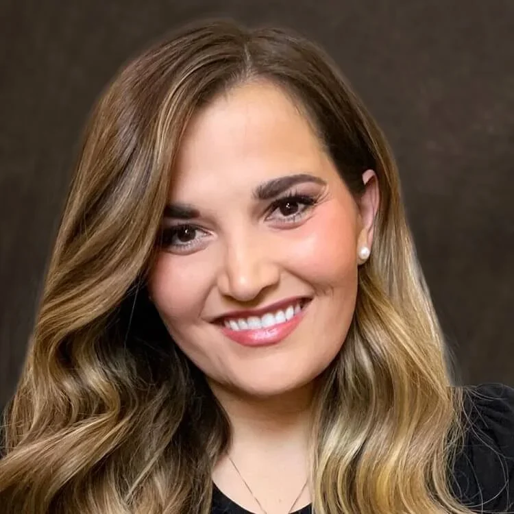 Close-up of a smiling woman with long wavy light brown hair, wearing pearl earrings and a black top.