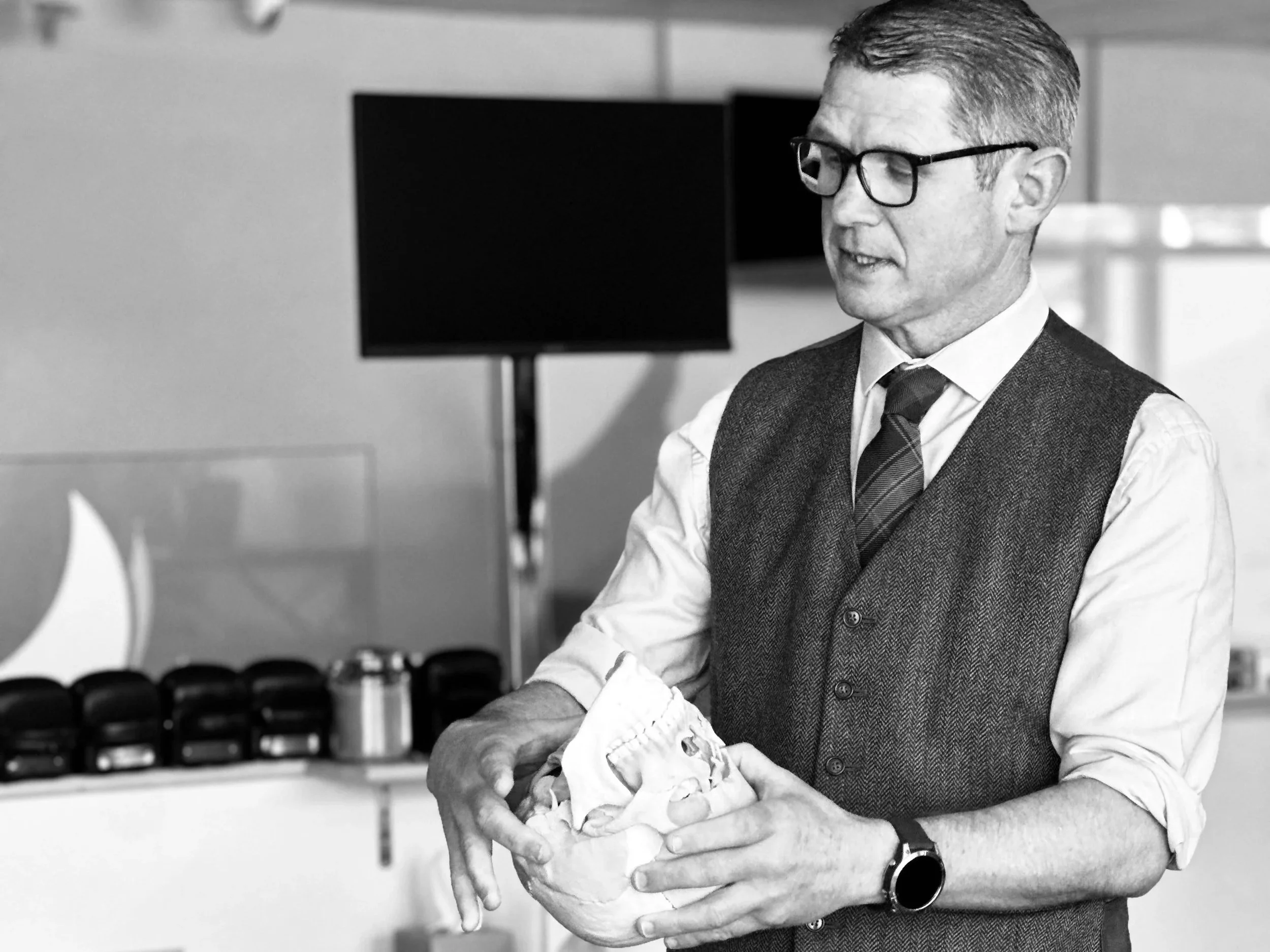 Empty auditorium filled with wooden chairs, with a stage and a large screen in the background.