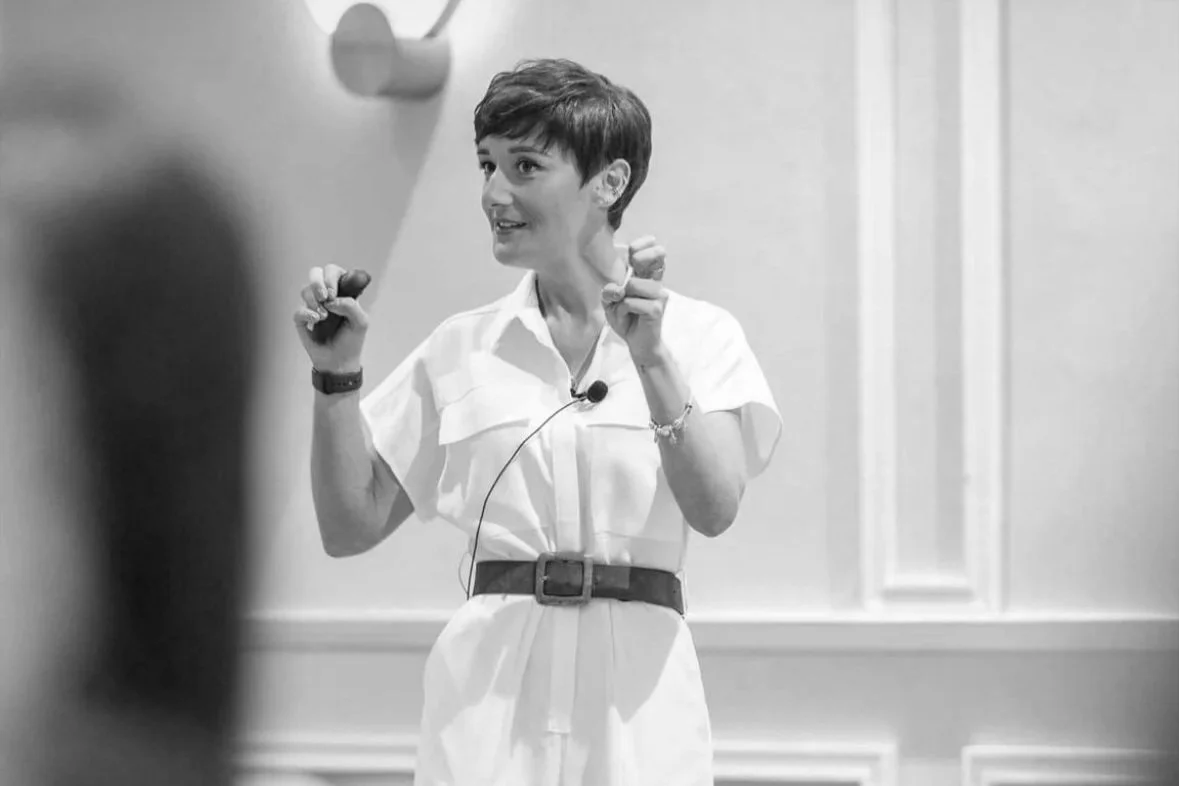 Two people exchanging a blank white sheet of paper in front of a window with a cityscape view.