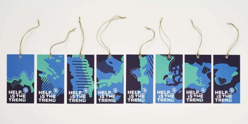 A series of eight rectangular tags with blue, green, and black abstract world map designs, each with the slogan 'Help is the trend,' attached to strings.