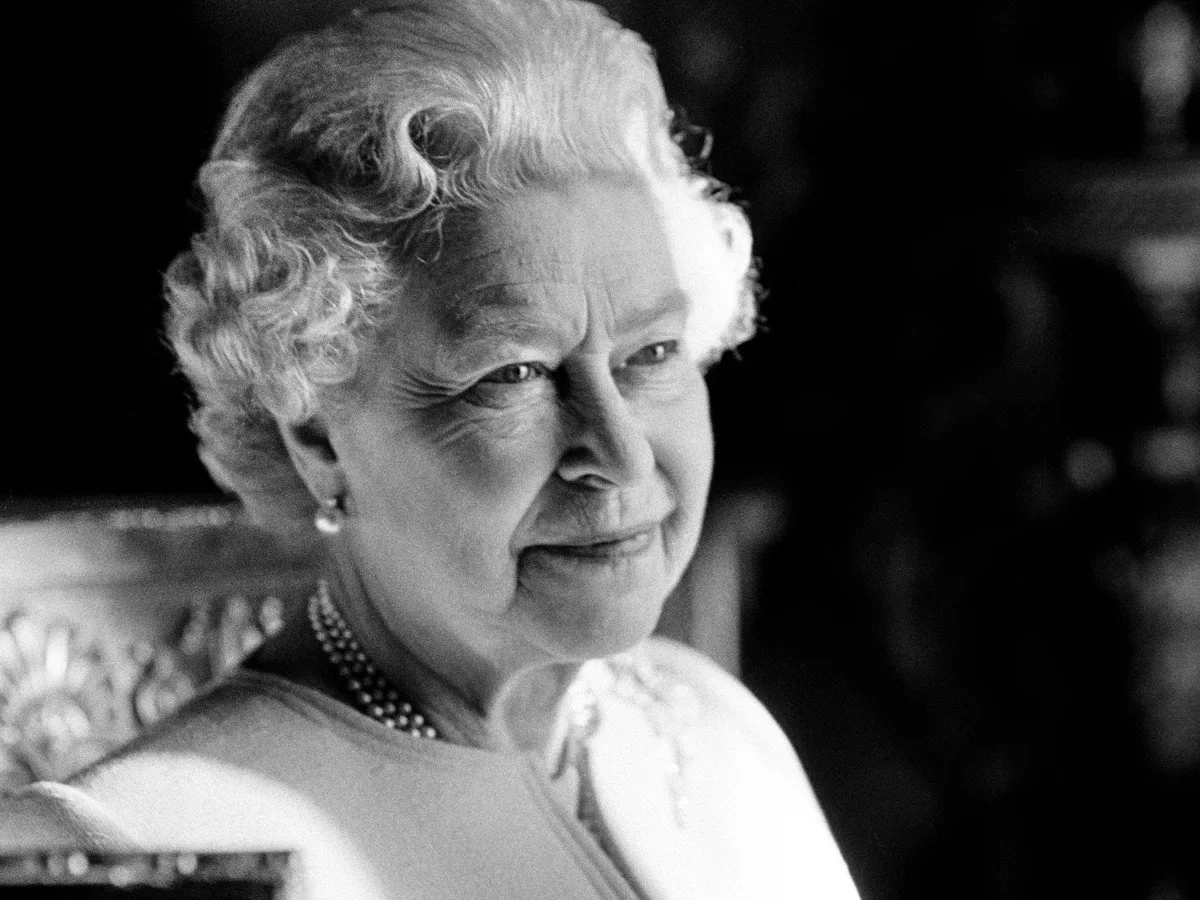 Black and white photo of Queen Elizabeth II smiling, wearing a pearl necklace and earrings.
