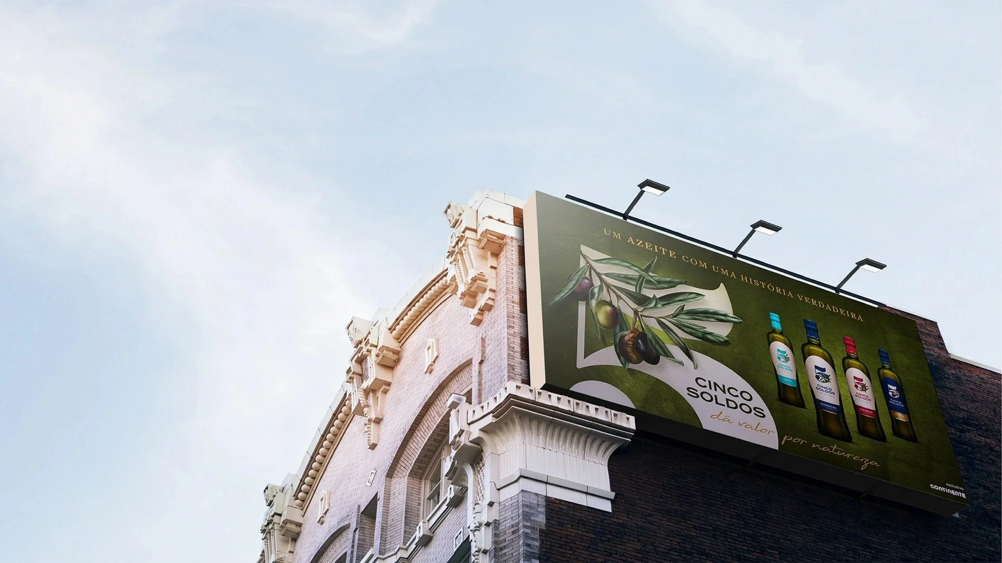 Billboard with an olive branch and bottles of olive oil, advertising a product called Cinco Soldo, with text in Portuguese and a light-colored historic building in the background.