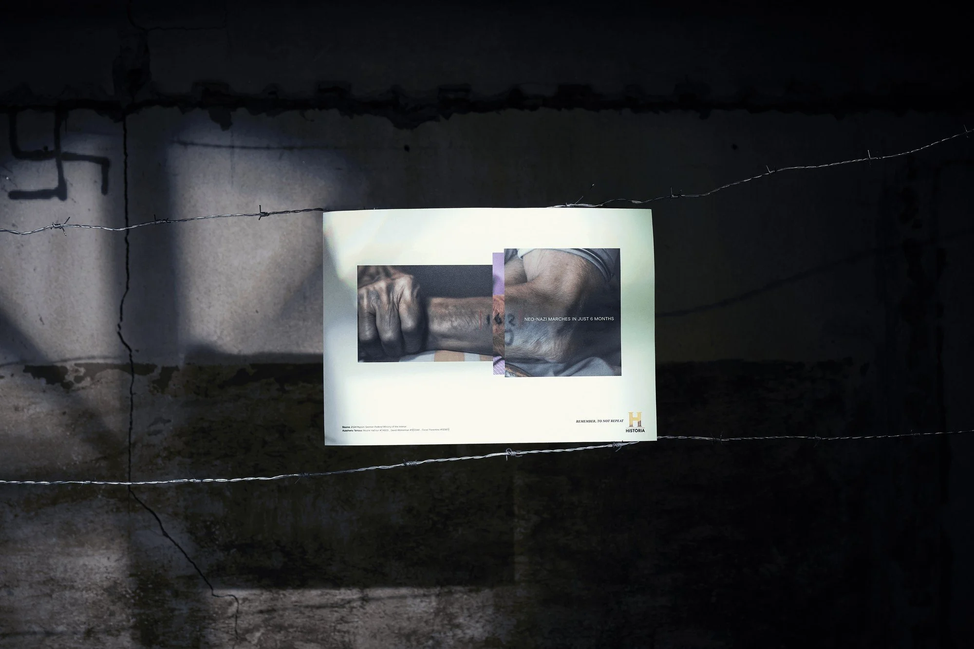 Photograph of a poster on a wire fence showing two hands, one grasping the wrist of the other, with text about a neo-Nazi march.