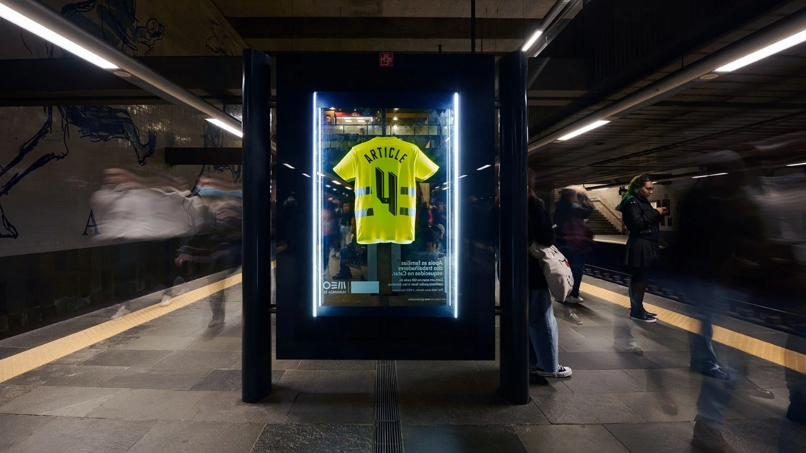 A yellow sports jersey with the name "ARTICLE" and the number "44" is displayed inside a glass case on a subway platform, with blurred pedestrians walking by.