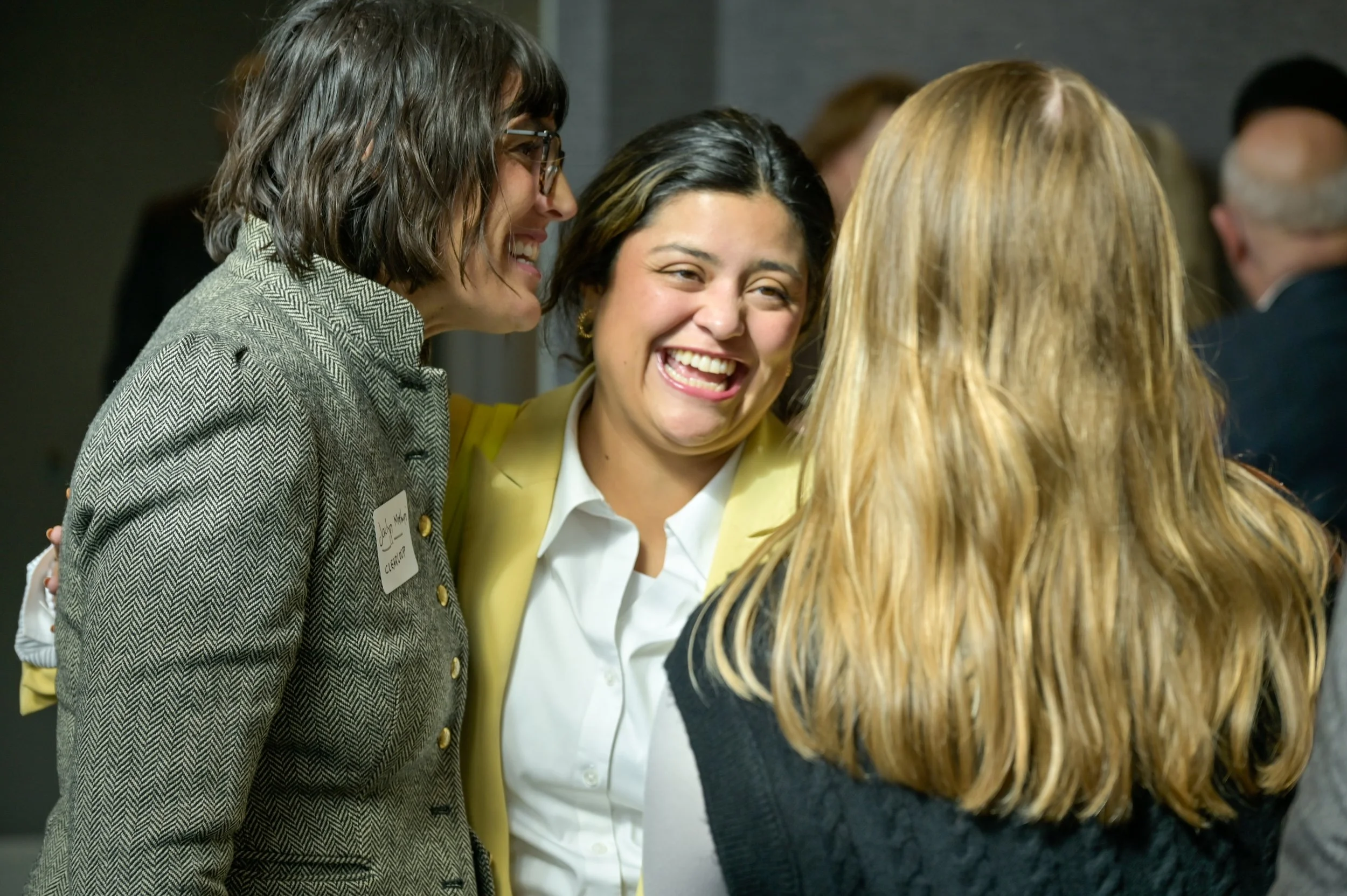 Three women smiling and talking at a social gathering or event.
