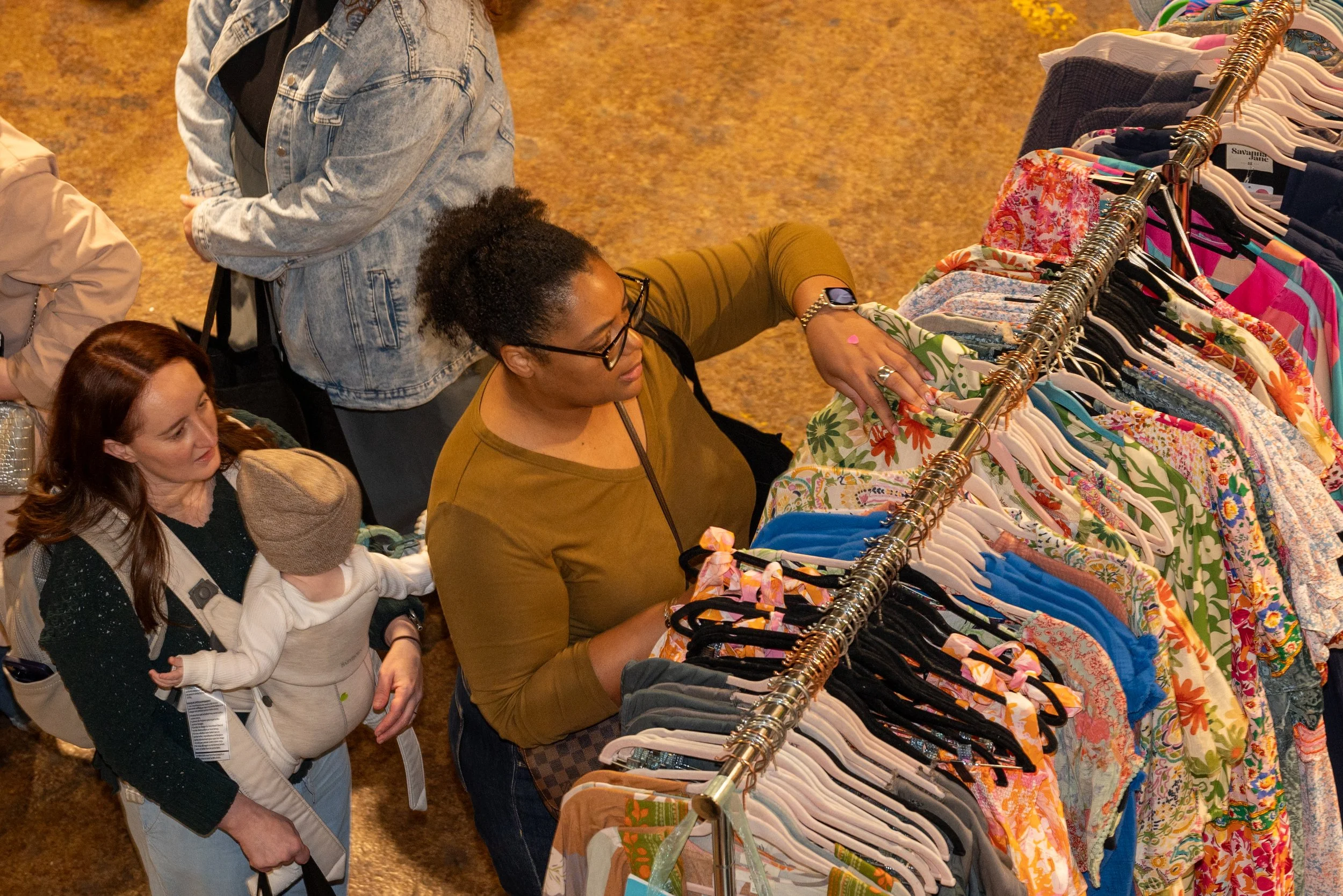 People shopping at a clothing rack with various colorful garments.