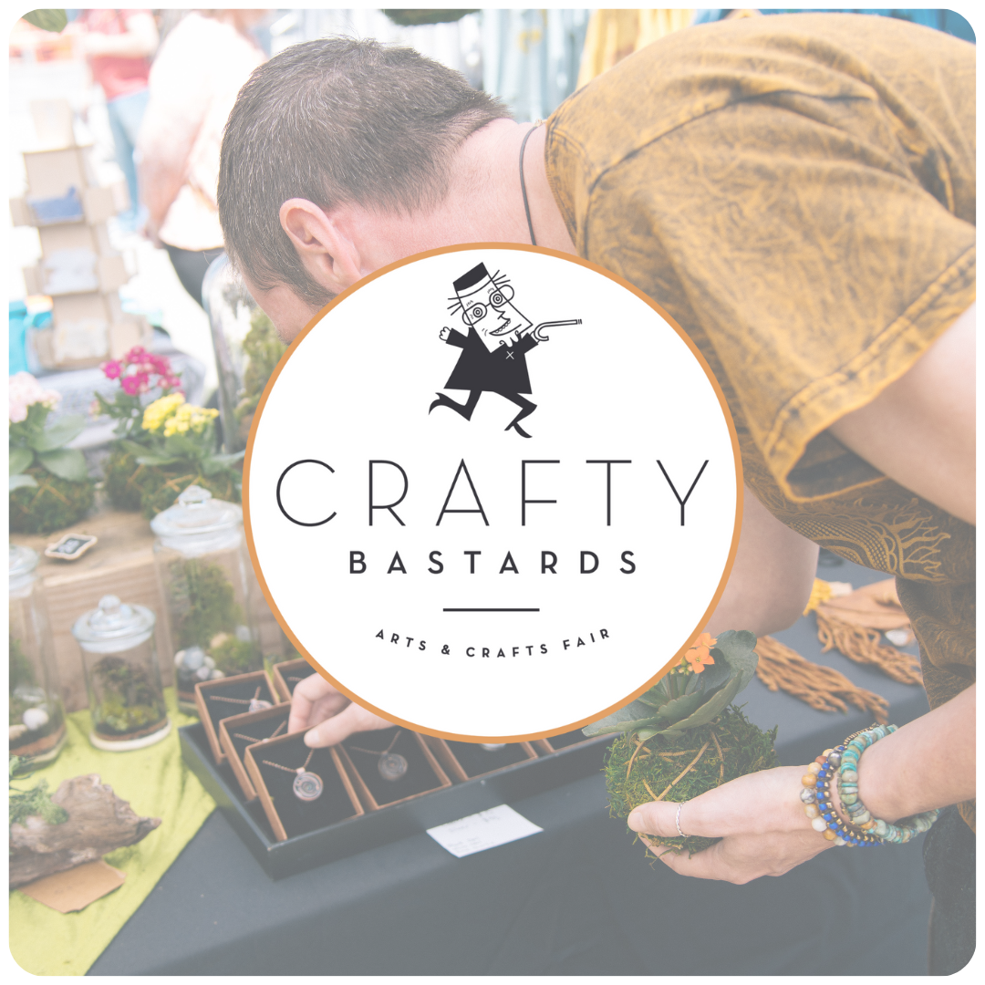 A person browsing handmade jewelry and crafts at an arts and crafts fair, with a round logo overlay that reads "Crafty Bastards Arts & Crafts Fair".
