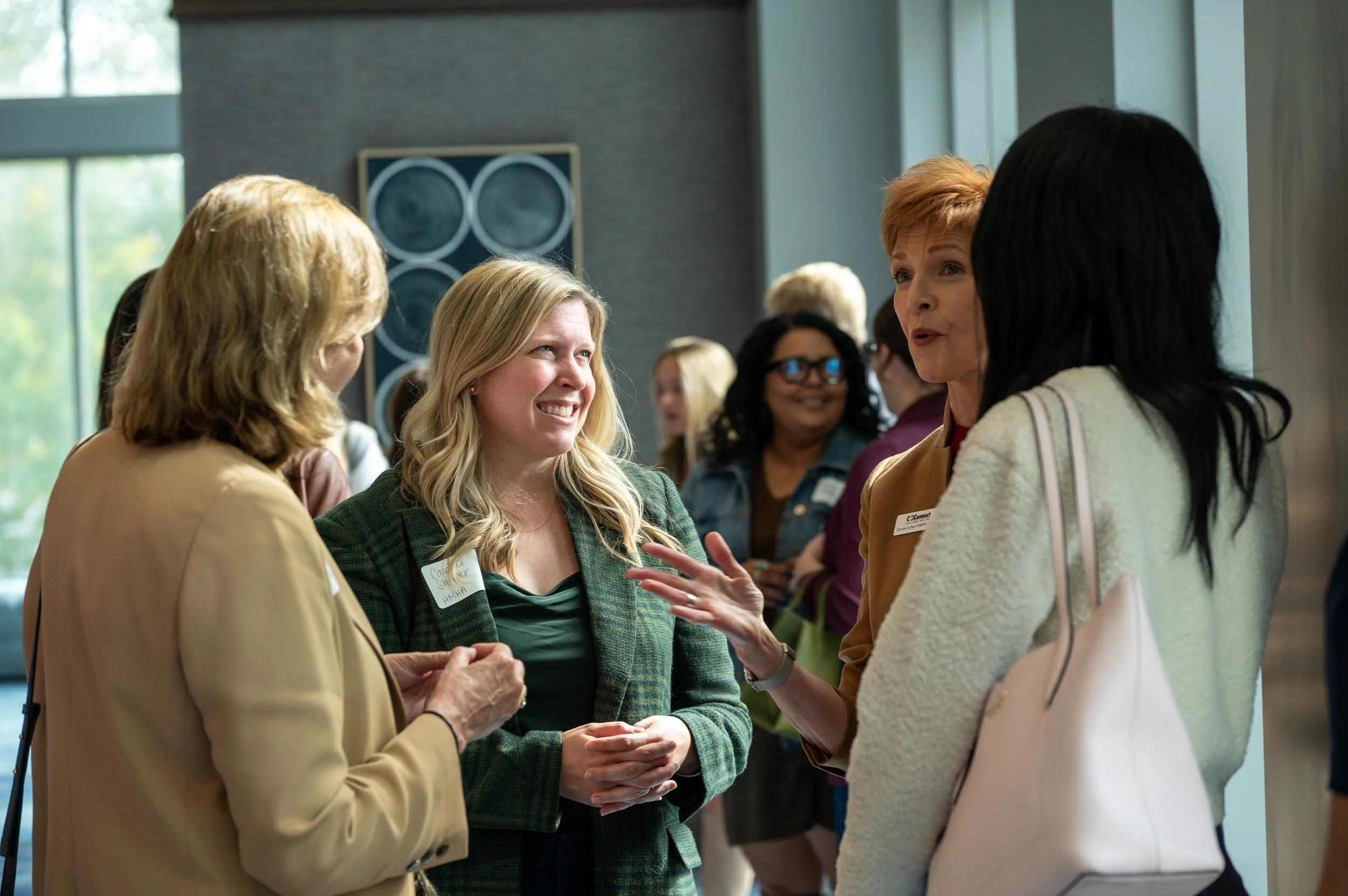 Group of women having a conversation at an indoor event, with some wearing conference badges.