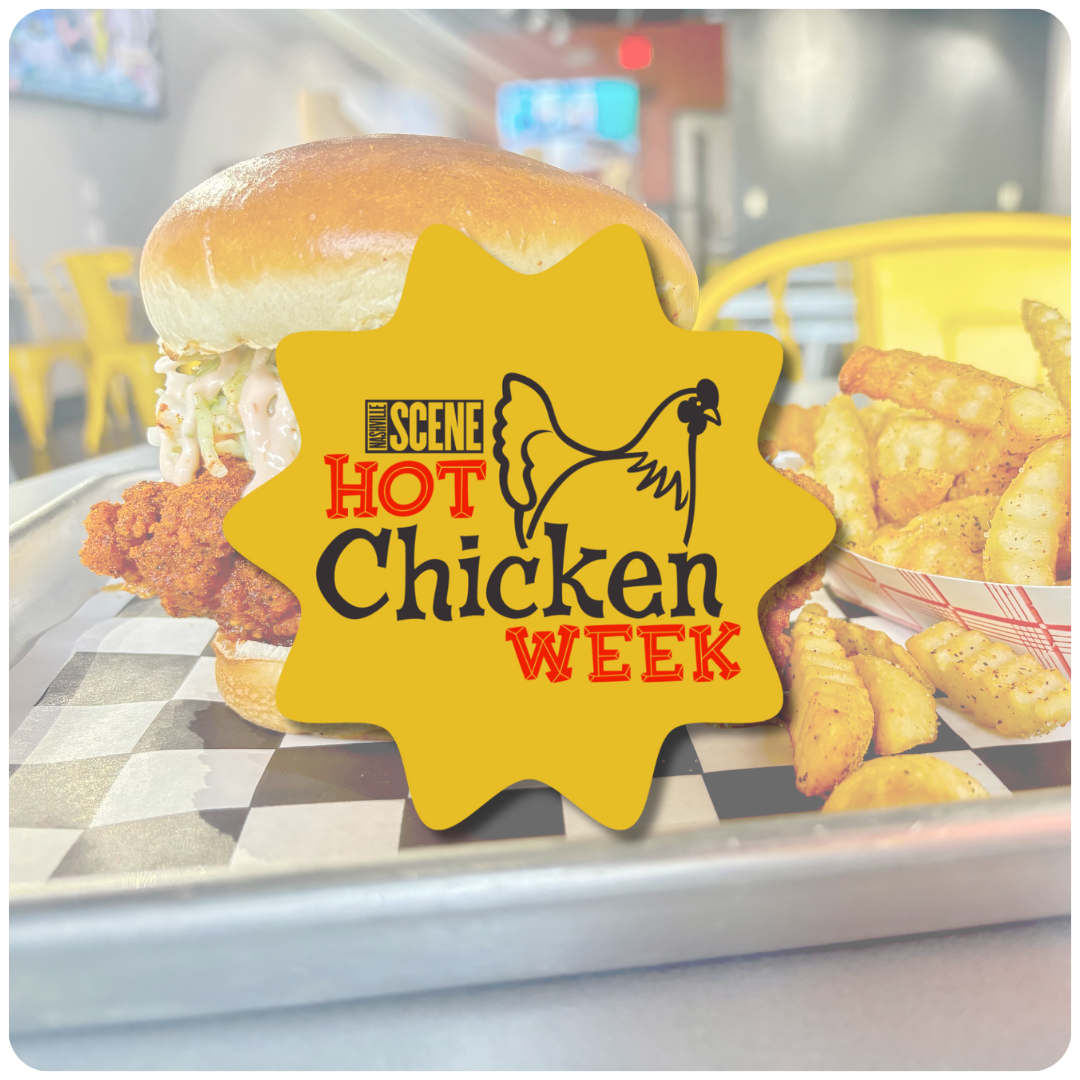 A fried chicken sandwich with mayonnaise, lettuce, and a bun, served on a checkered paper with a side of crinkle-cut fries in a red checkered basket. There is a yellow sign with a chicken illustration and the text 'Hot Chicken Week' in front of the s