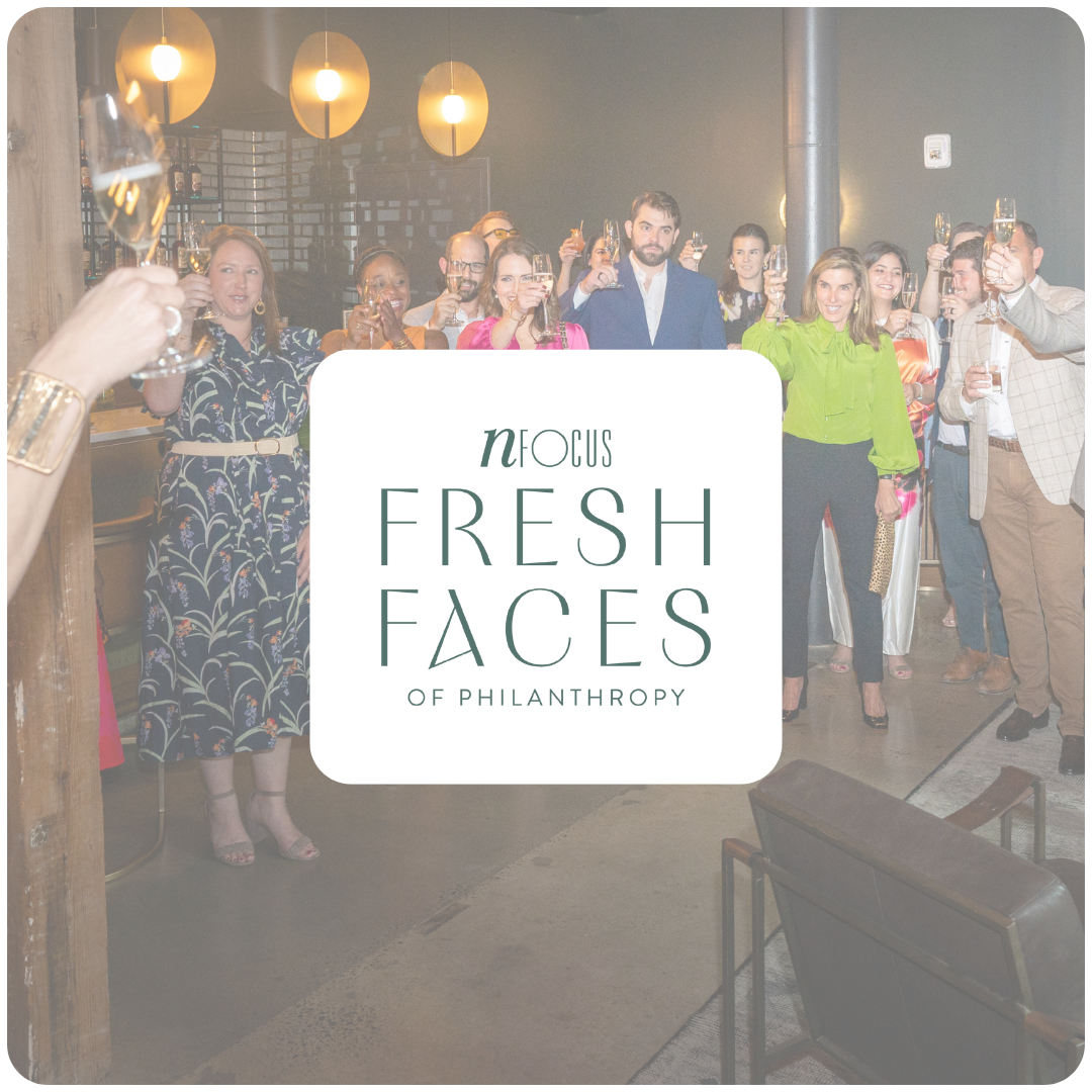 A group of people at a celebration raising glasses in a toast with a sign in the front that says 'Focus on Fresh Faces of Philanthropy'.