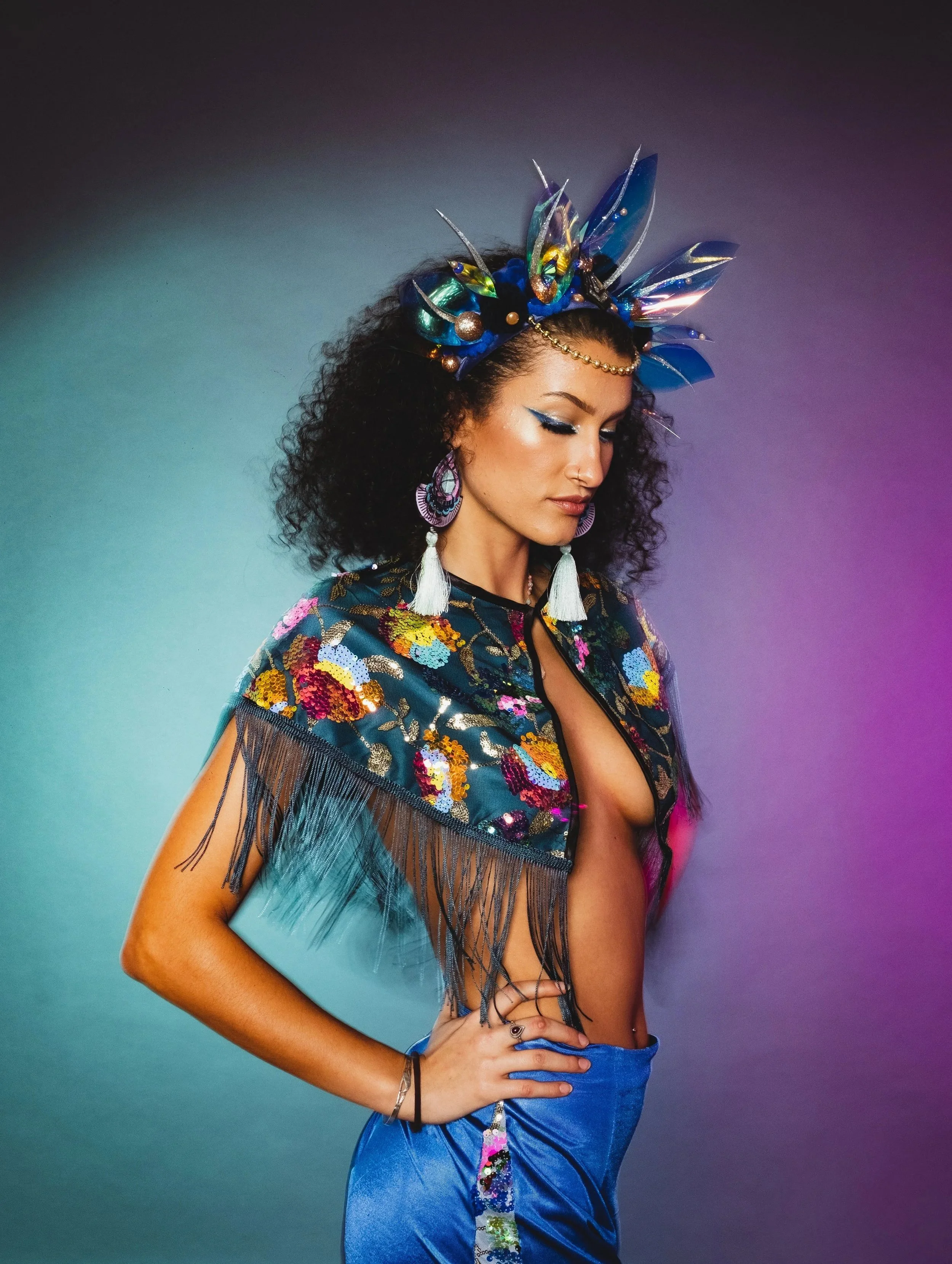 Woman wearing a colorful, decorative outfit with a feathered headpiece against a gradient background.
