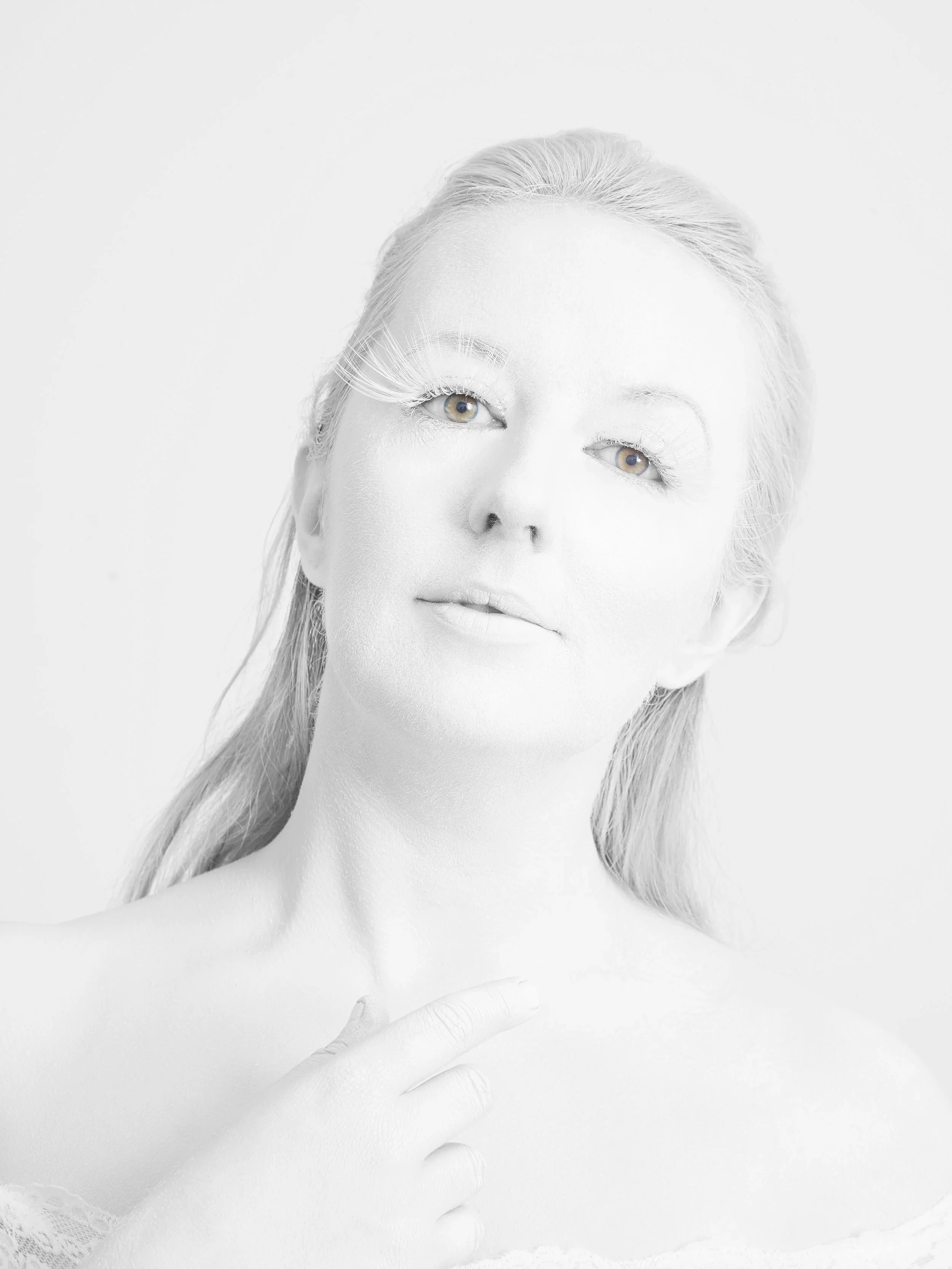 A black-and-white portrait of a woman with light-colored hair, pale skin, and light-colored eyes, looking softly at the camera with a gentle expression.