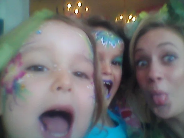 Three young girls with colorful face paint and makeup, making silly faces.