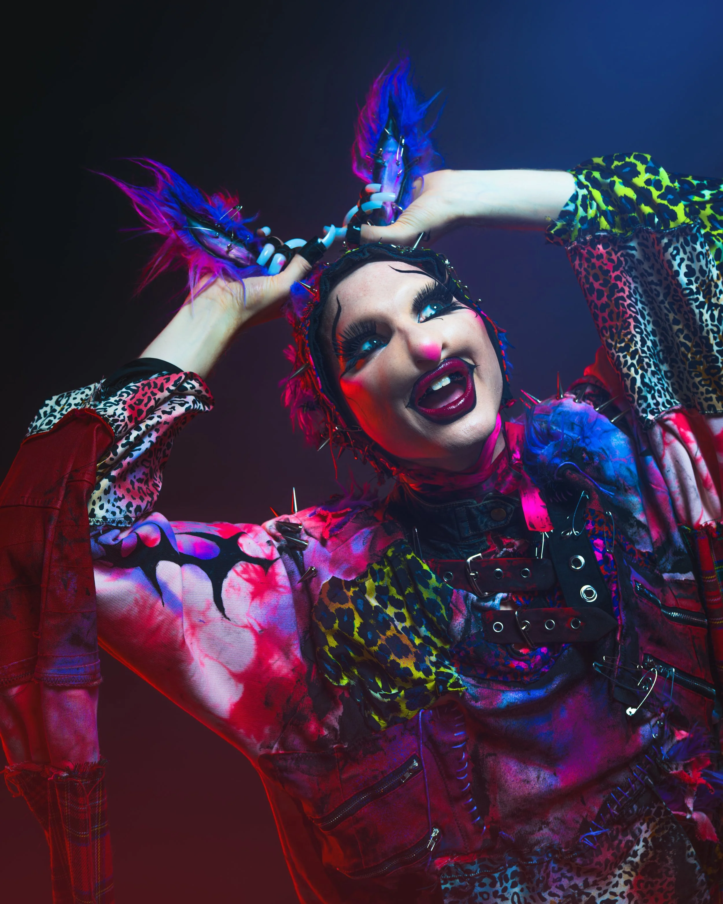 Person with vibrant makeup, colorful spiked hair accessories, and a punk-inspired outfit with leopard and camo patterns, posing with a playful expression.