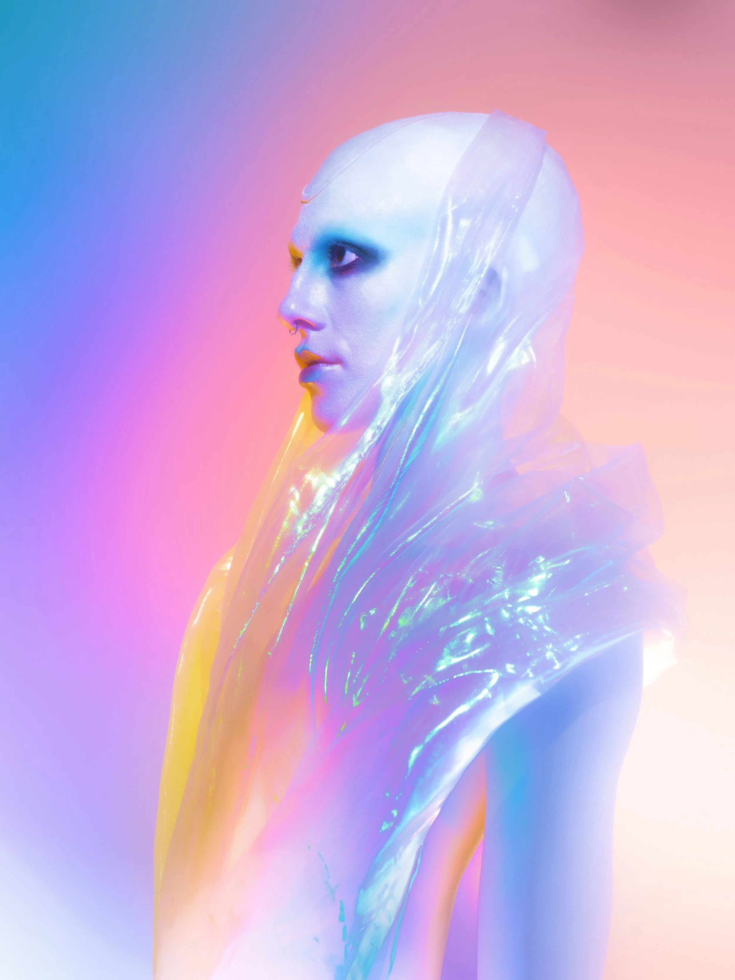 Side profile of a person with iridescent makeup and a translucent hood, set against a pastel rainbow background.
