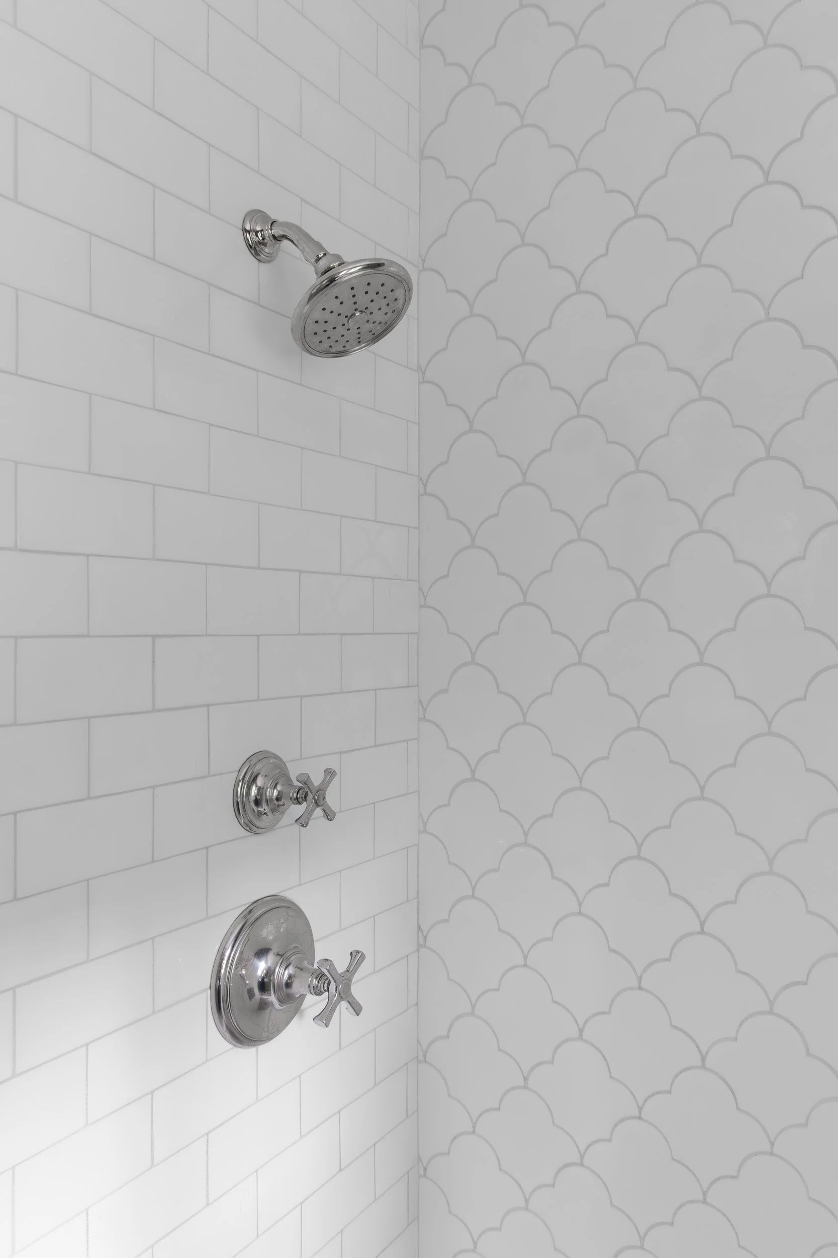 Silver shower head and controls on a white tiled wall in a shower.