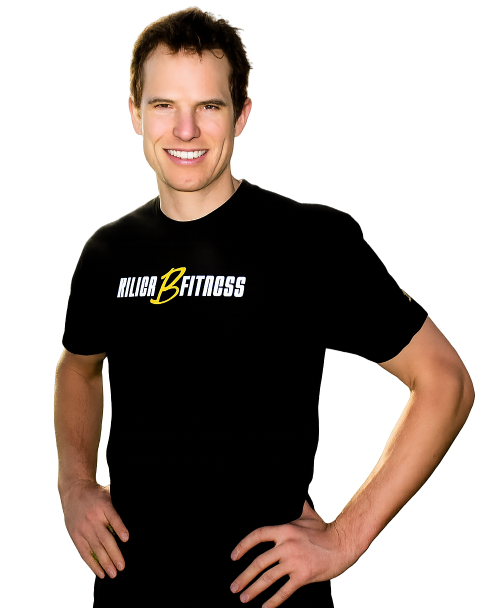 A smiling man with short brown hair, wearing a black T-shirt with the words "KILOR B FITNESS" printed on it, standing with hands on hips against a plain black background.