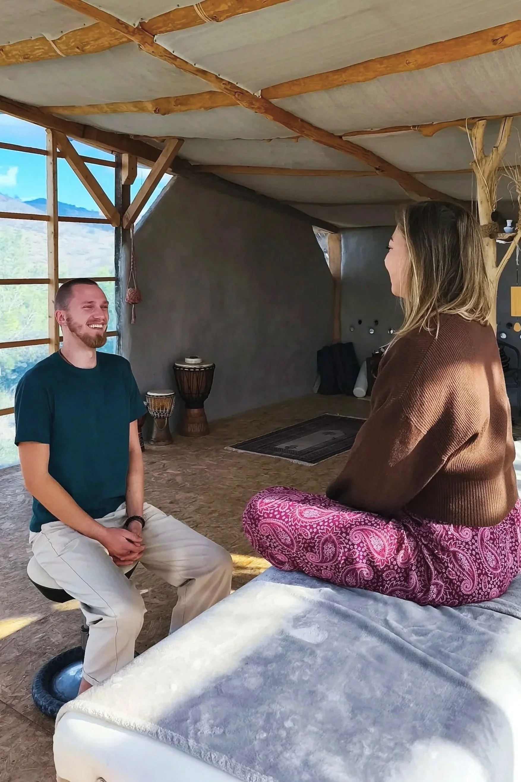 Zwei Menschen sitzen in einem natürlichen Raum, lachen und unterhalten sich.