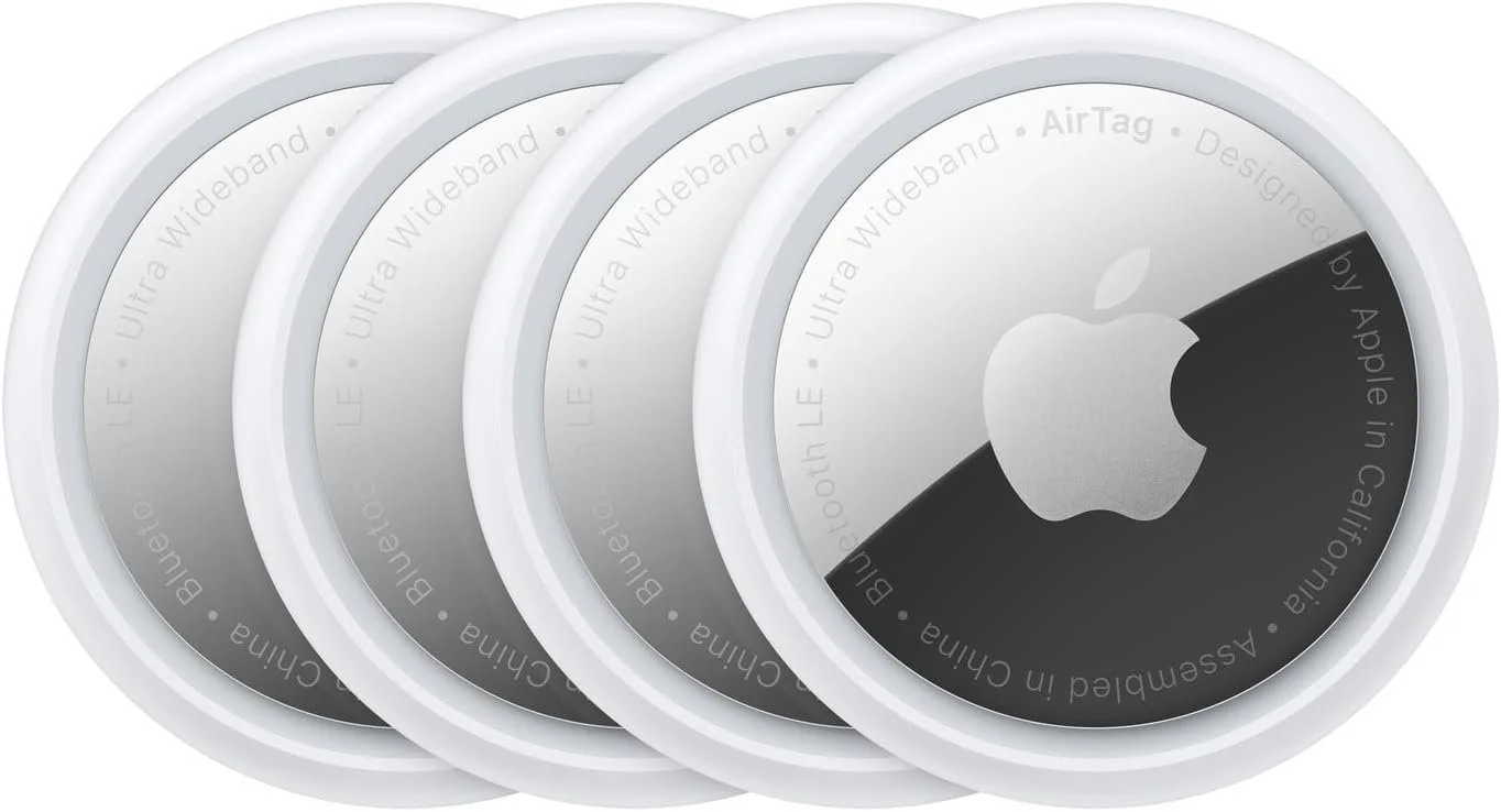 Four Apple AirTags with white circular plastic casing and black and white Apple logo on the top, arranged in a row.