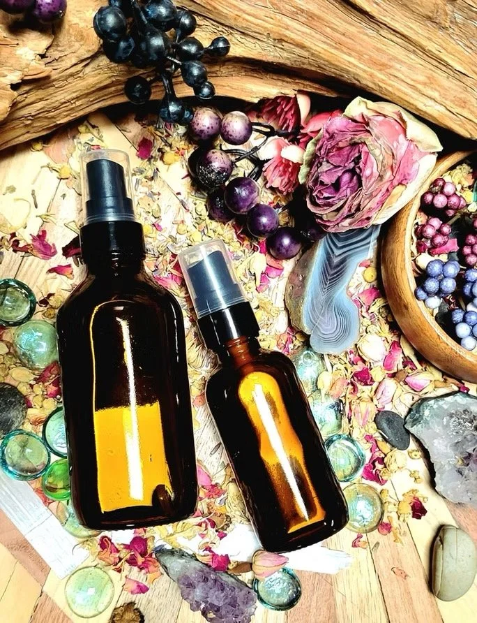 Amber glass spray bottles of herbal facial toner surrounded by dried flowers and botanicals in natural skincare setting