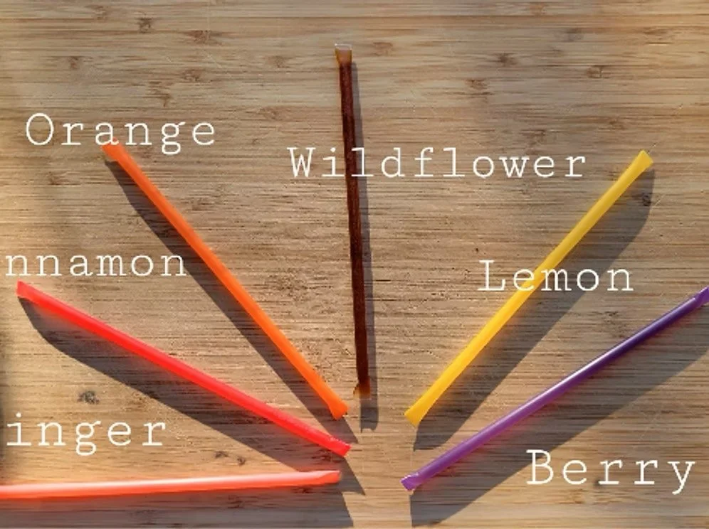 Assorted flavored honey sticks labeled with flavors including wildflower, lemon, berry, and orange